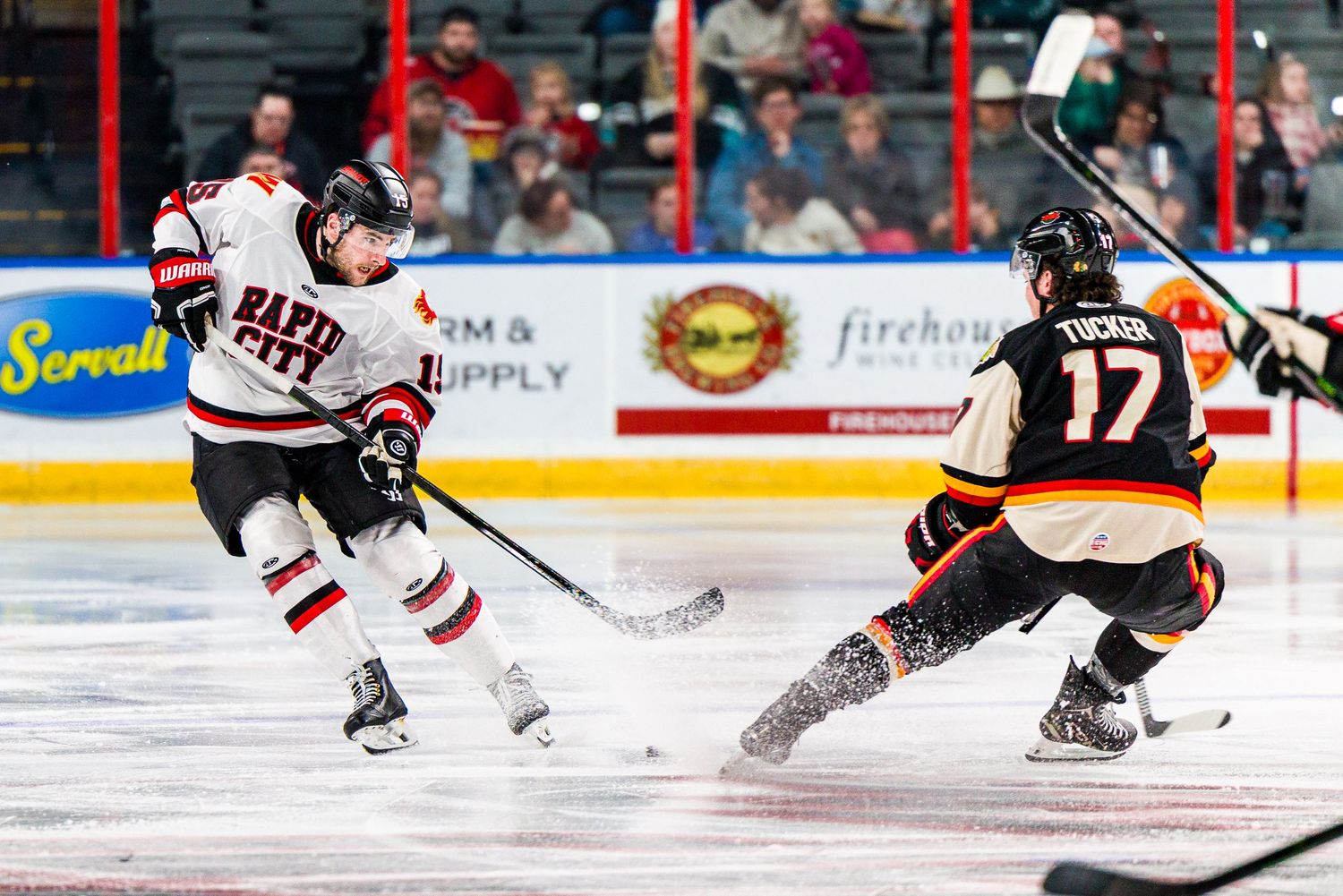 Two hockey players in action on the ice during a competitive match, one in red and white, one in black and orange.