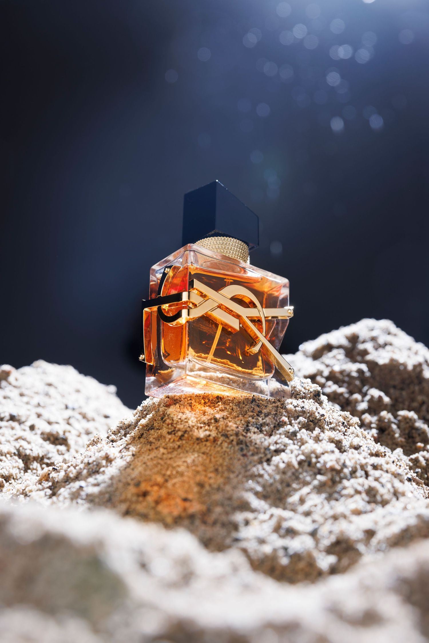 Orange perfume bottle nestled in white powder photographed from multiple angles.