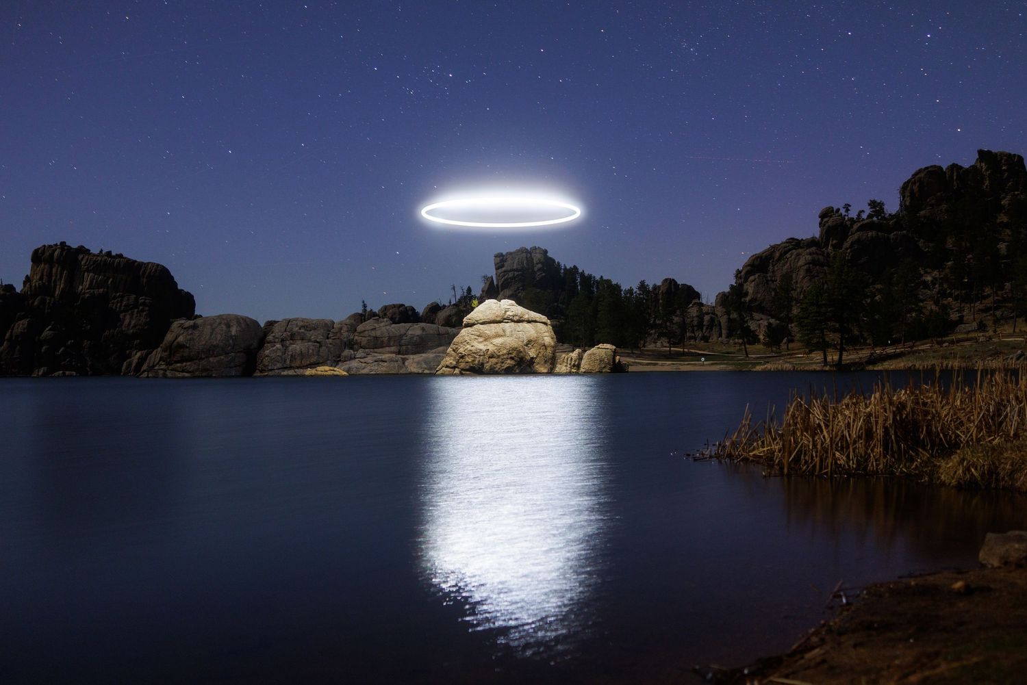 Glowing orb reflects on lake surface near rocky shoreline at night.