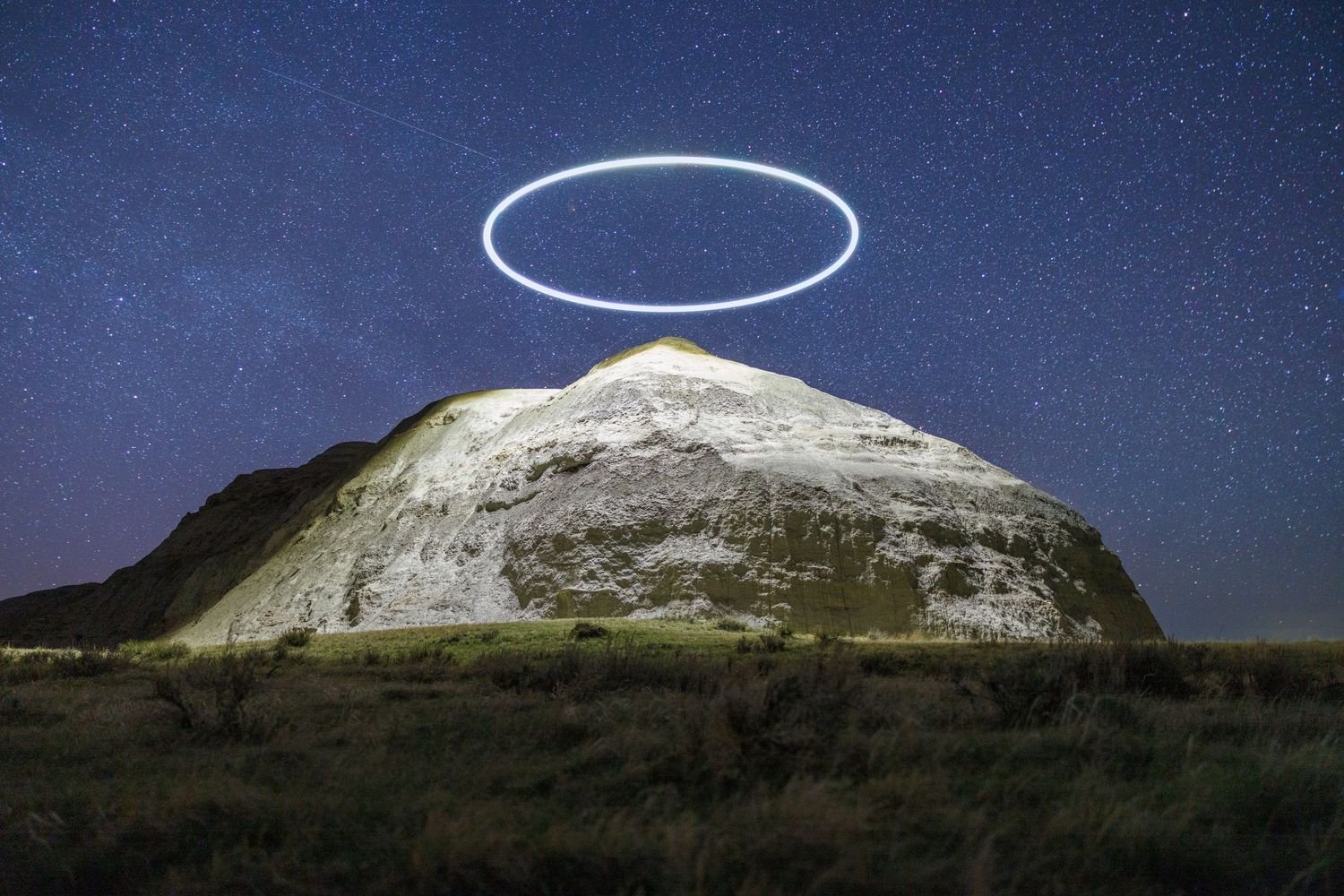 Bright circular light phenomenon illuminates mountain landscape under starry night sky.