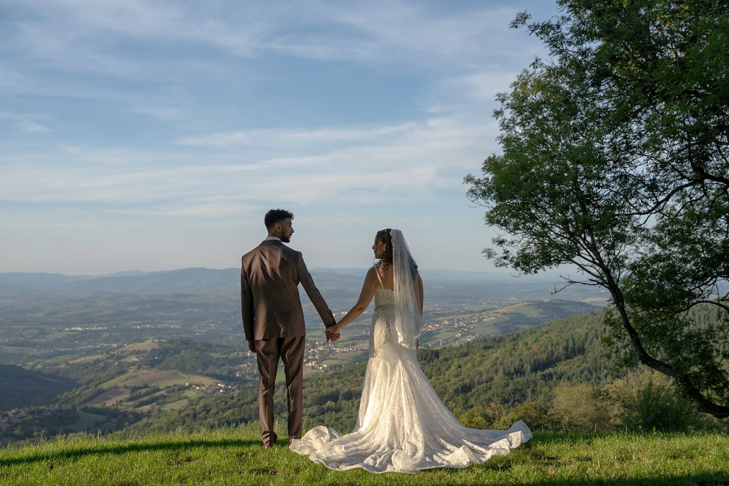 Scenic mountaintop wedding photos showcase couple in elegant attire against a backdrop of rolling hills and blue skies.