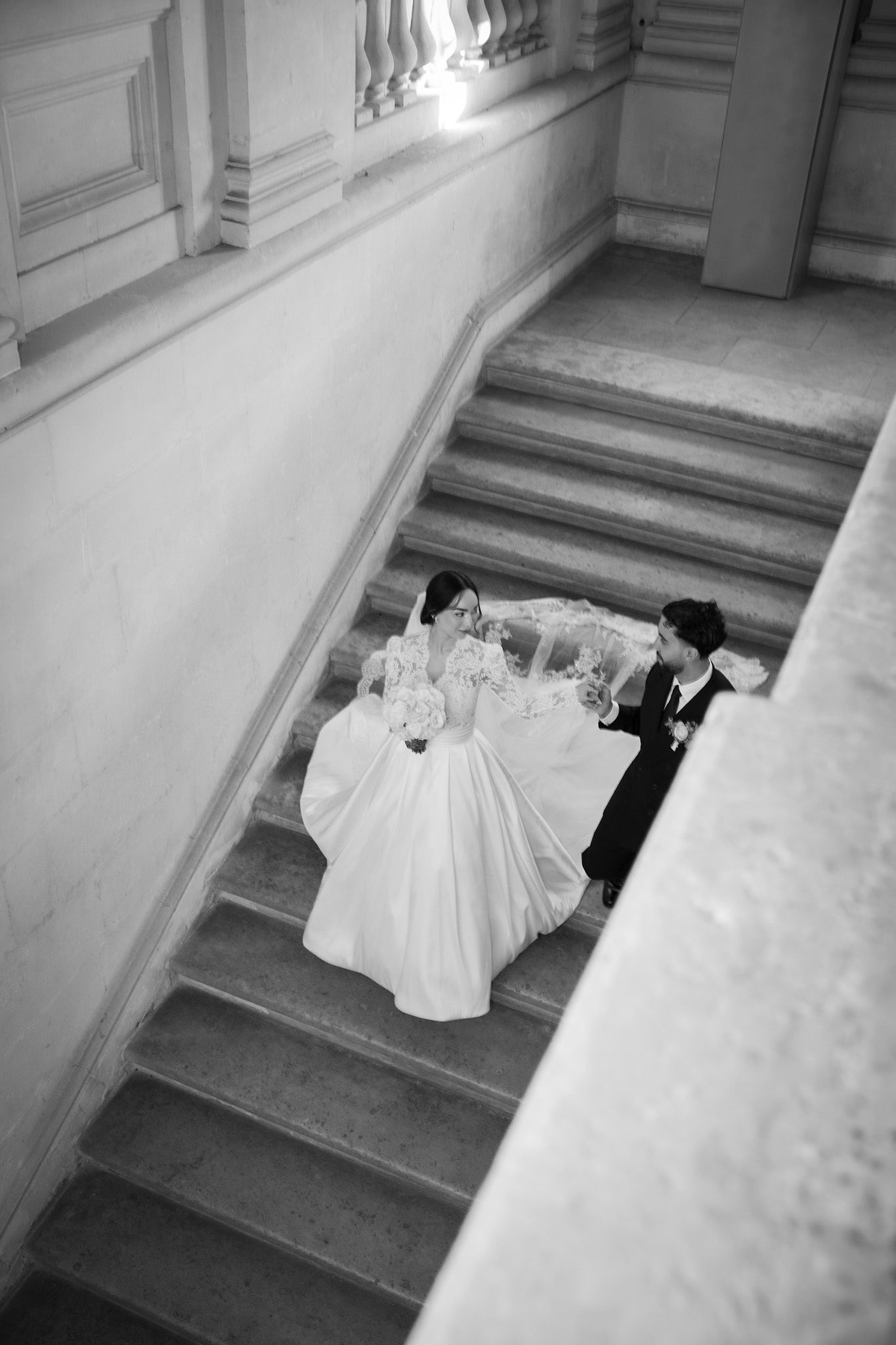 Black and white aerial view of bride and groom walking up grand staircase on wedding day.