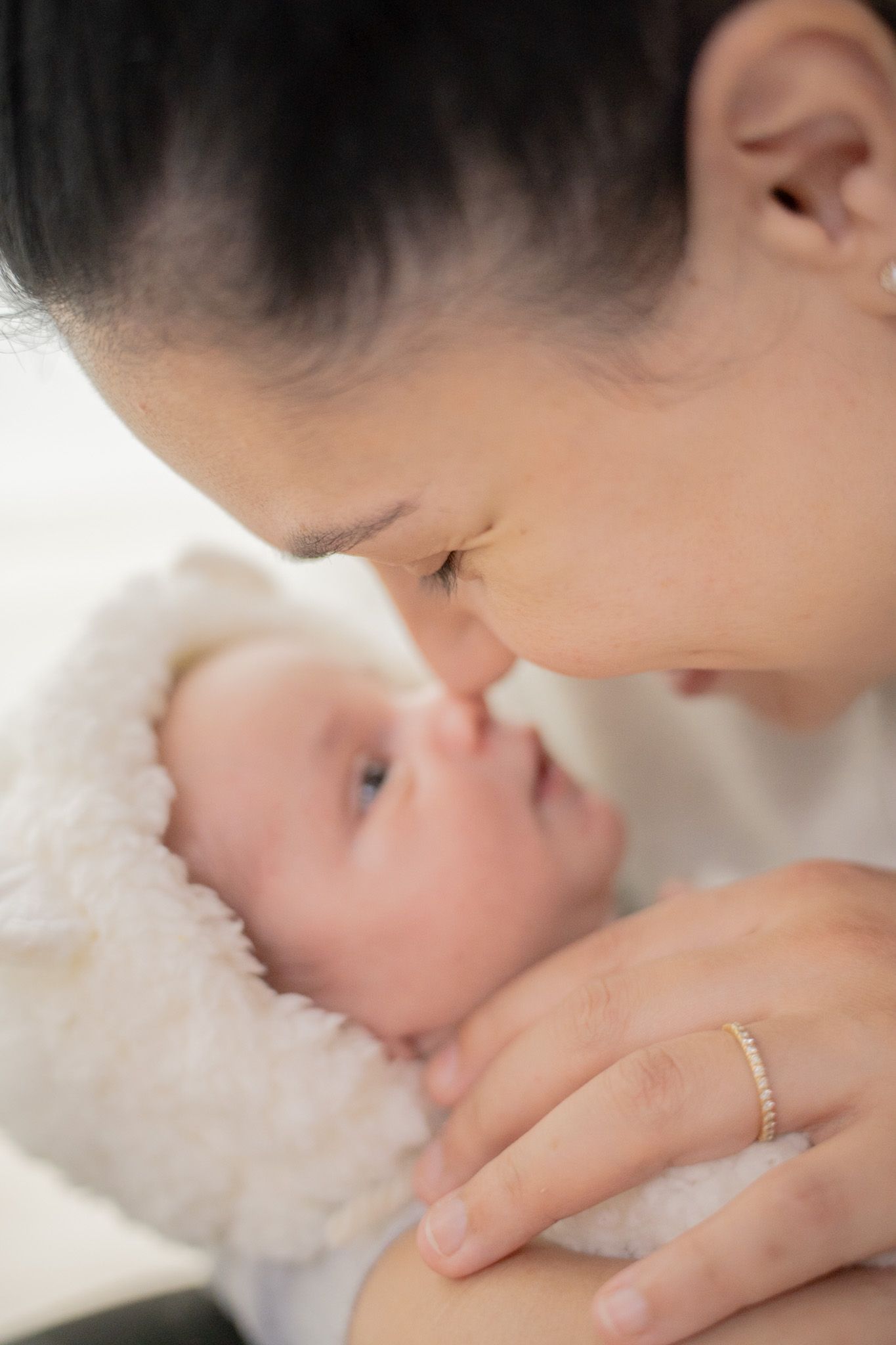 A tender moment between parent and baby as they share a gentle close-up interaction on soft white fabric.