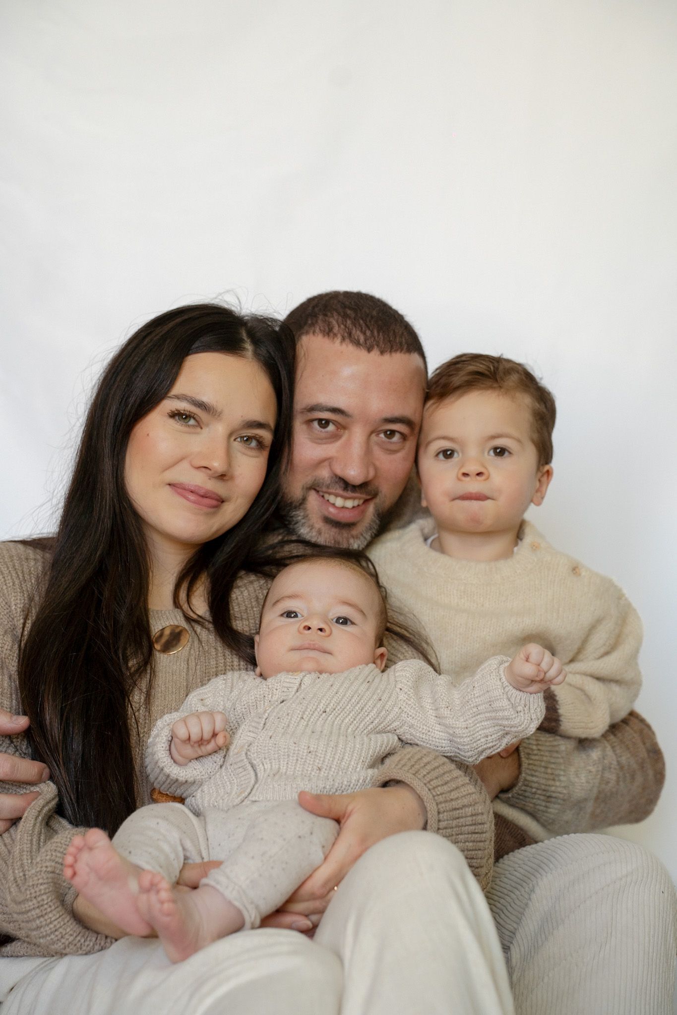 A family poses together wearing cream colored sweaters in a series of intimate portrait photographs.