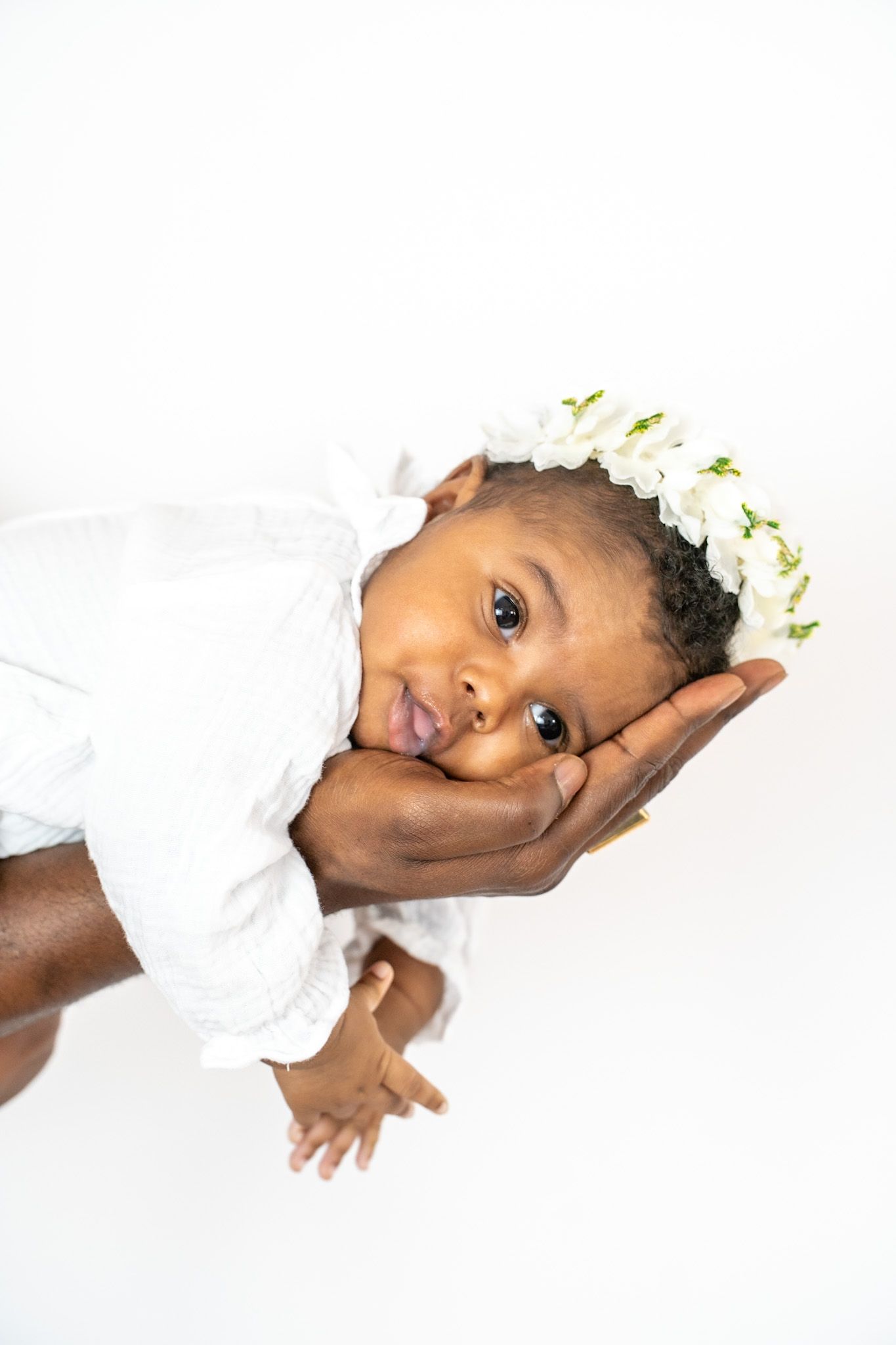 A young baby wearing white clothing lays on their side while resting on a white surface.