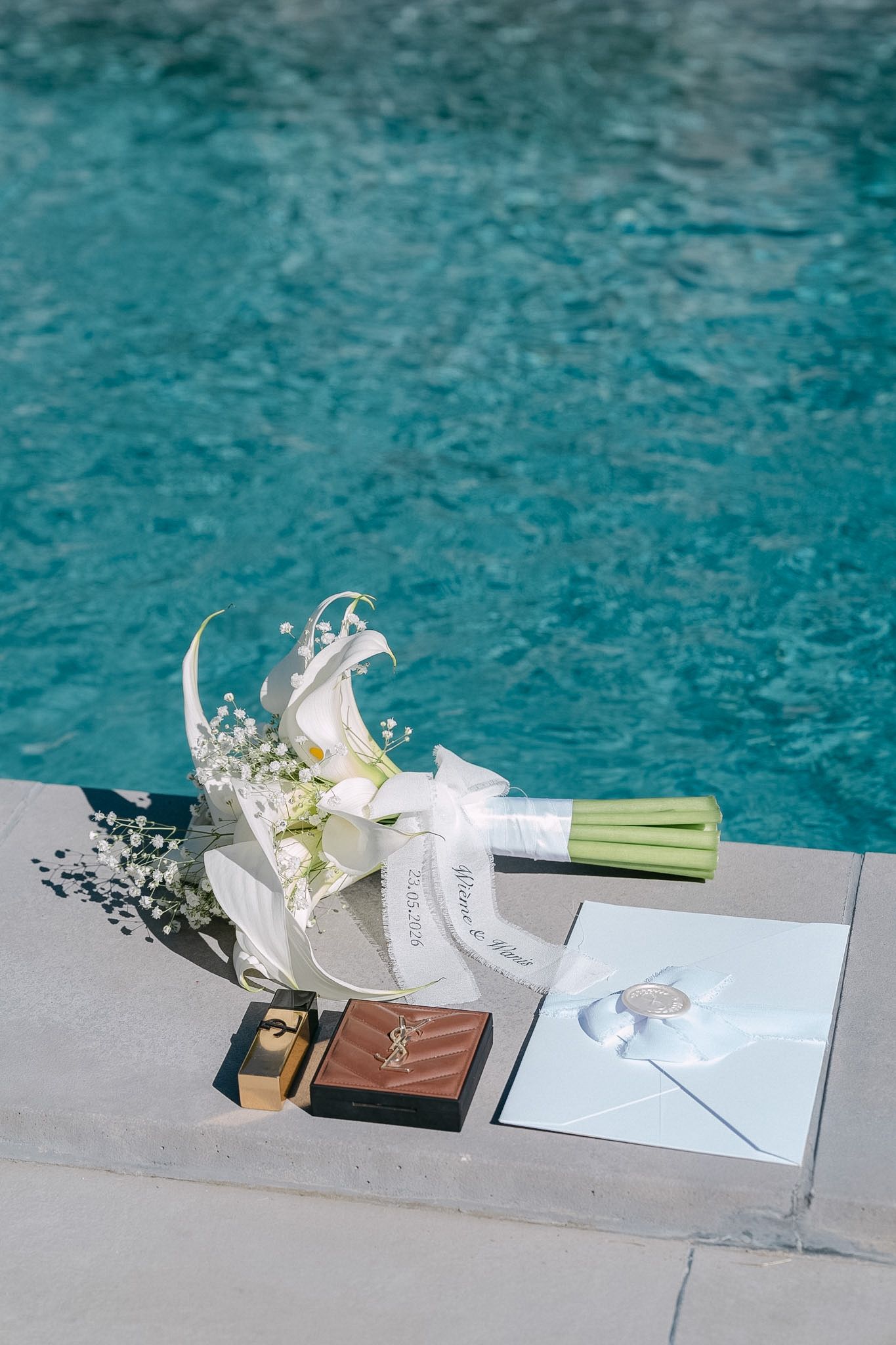 White wedding bouquet with lilies and rings beside a pool.