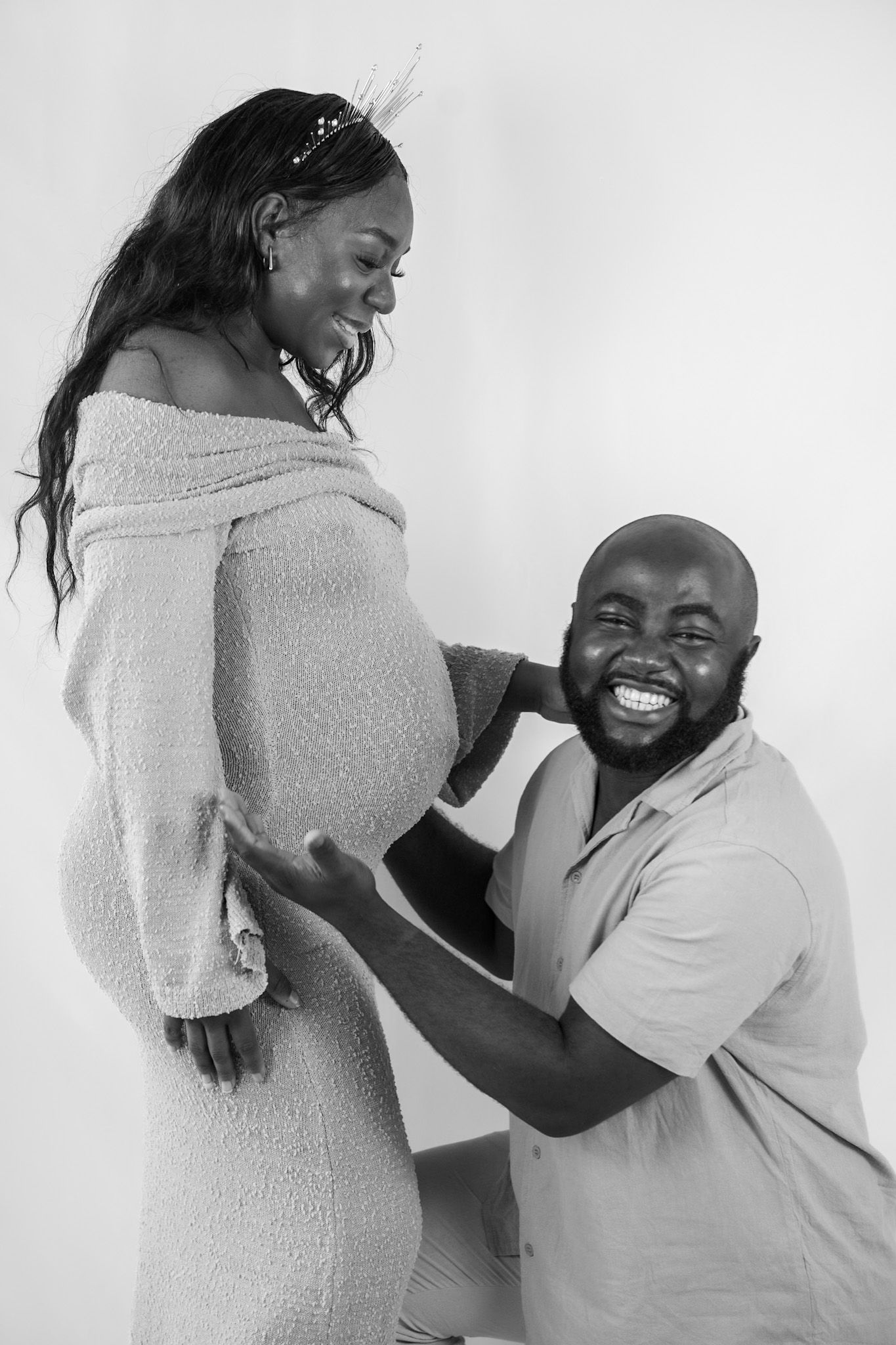 A joyful maternity photo session showing a couple embracing and laughing together against a white backdrop.