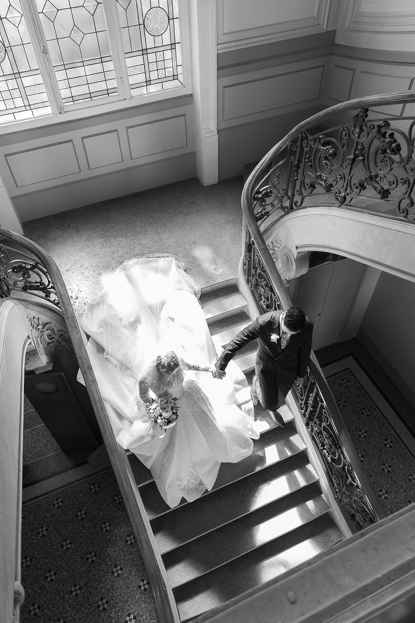 Aerial black and white view of bride and groom on grand staircase with iron railings.