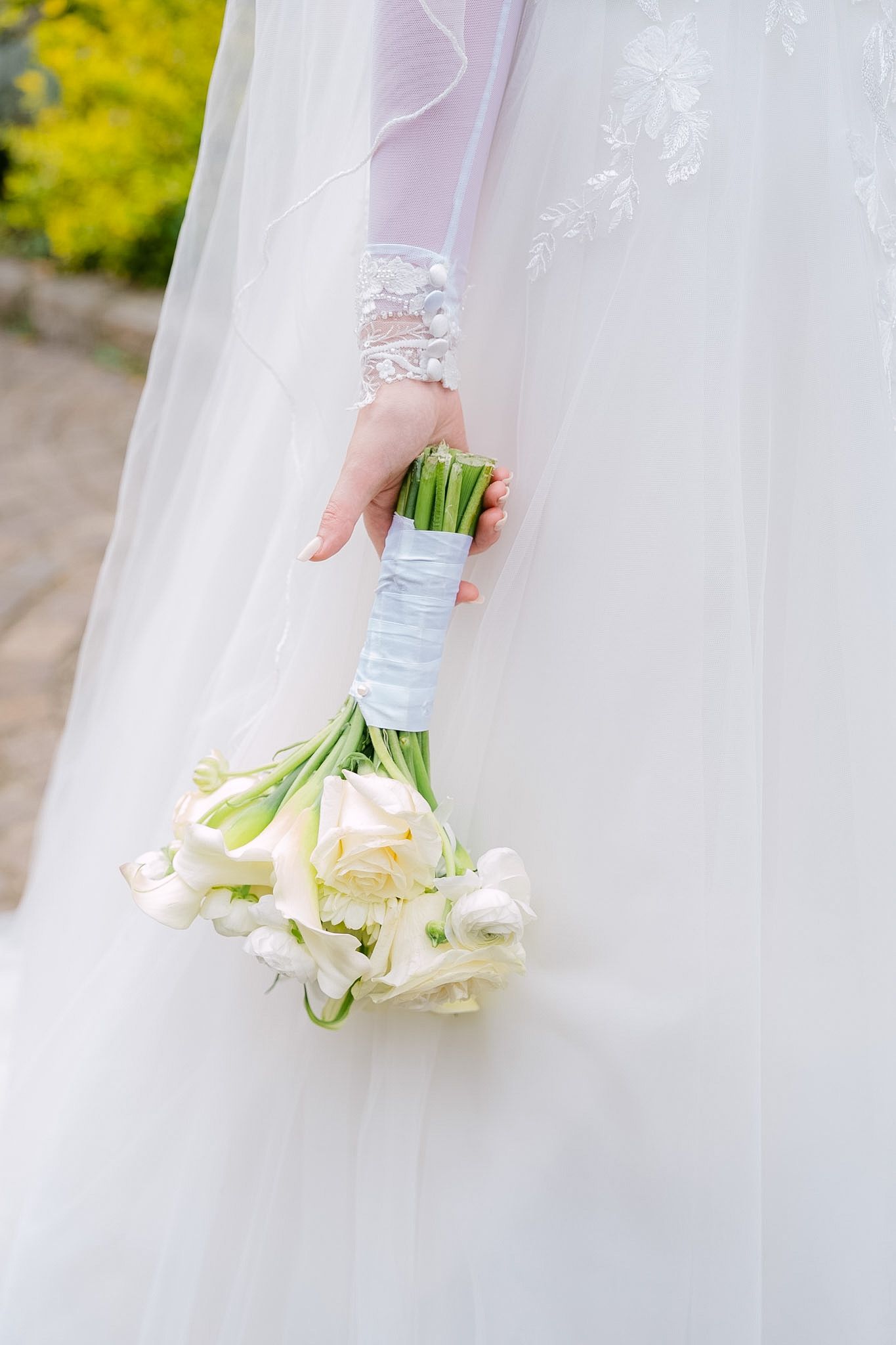 Bride in white lace wedding dress holding elegant bouquet of white tulips wrapped with light blue ribbon.