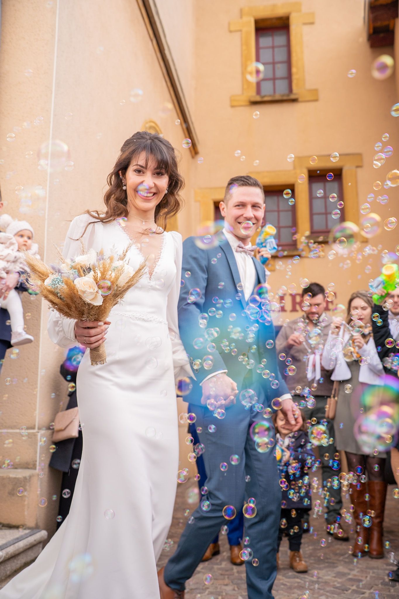 Joyful wedding sequence with soap bubbles floating around couple outside yellow building.