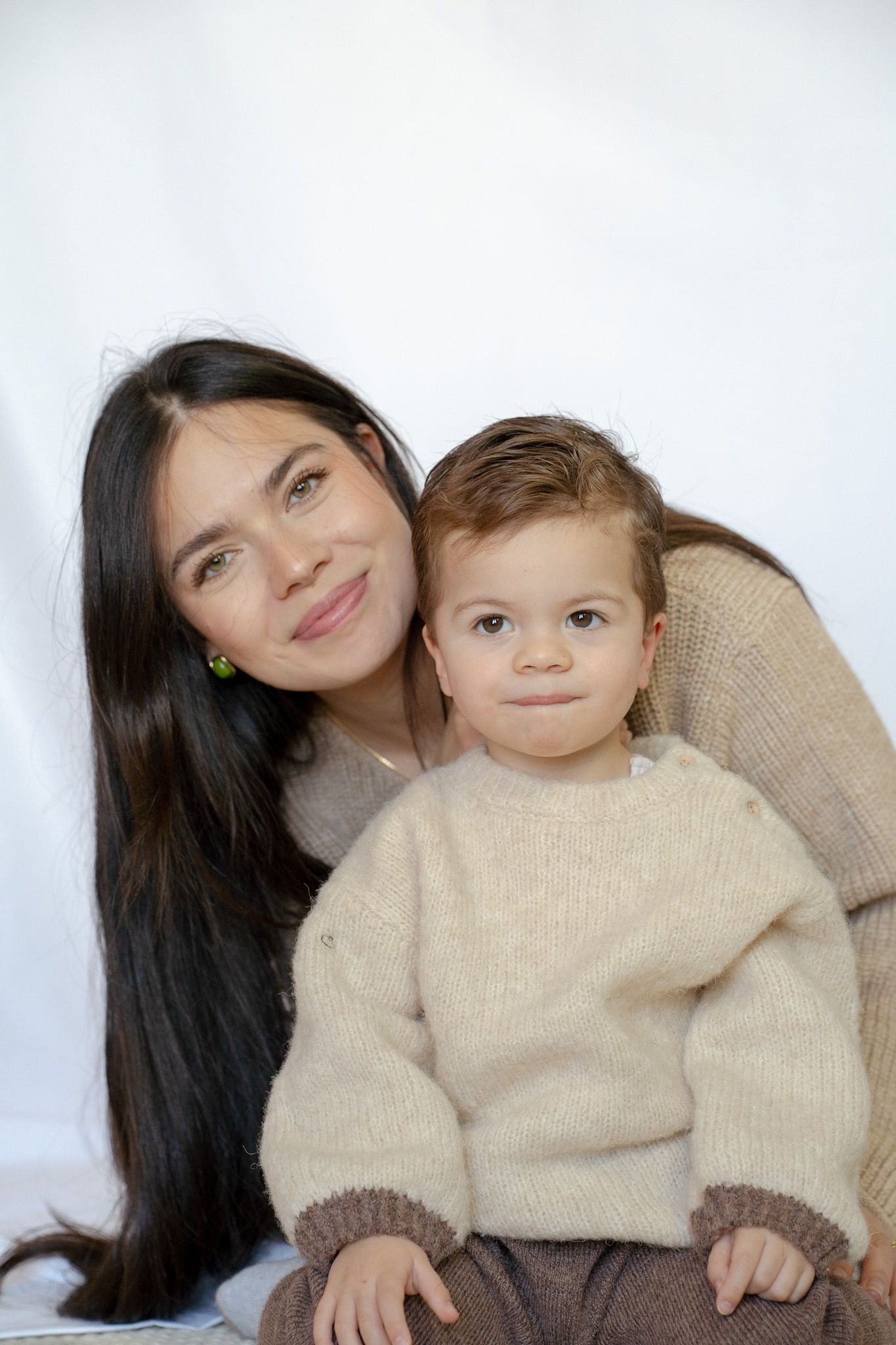 Two people wearing beige sweaters pose together against a white background in a series of casual portraits.