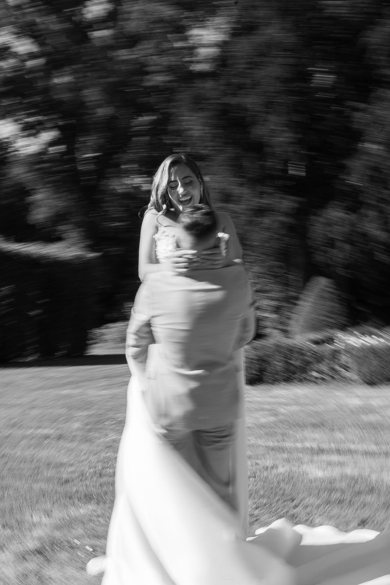 Black and white photo of a bride and groom spinning joyfully outdoors, with motion blur capturing their wedding day celebration.