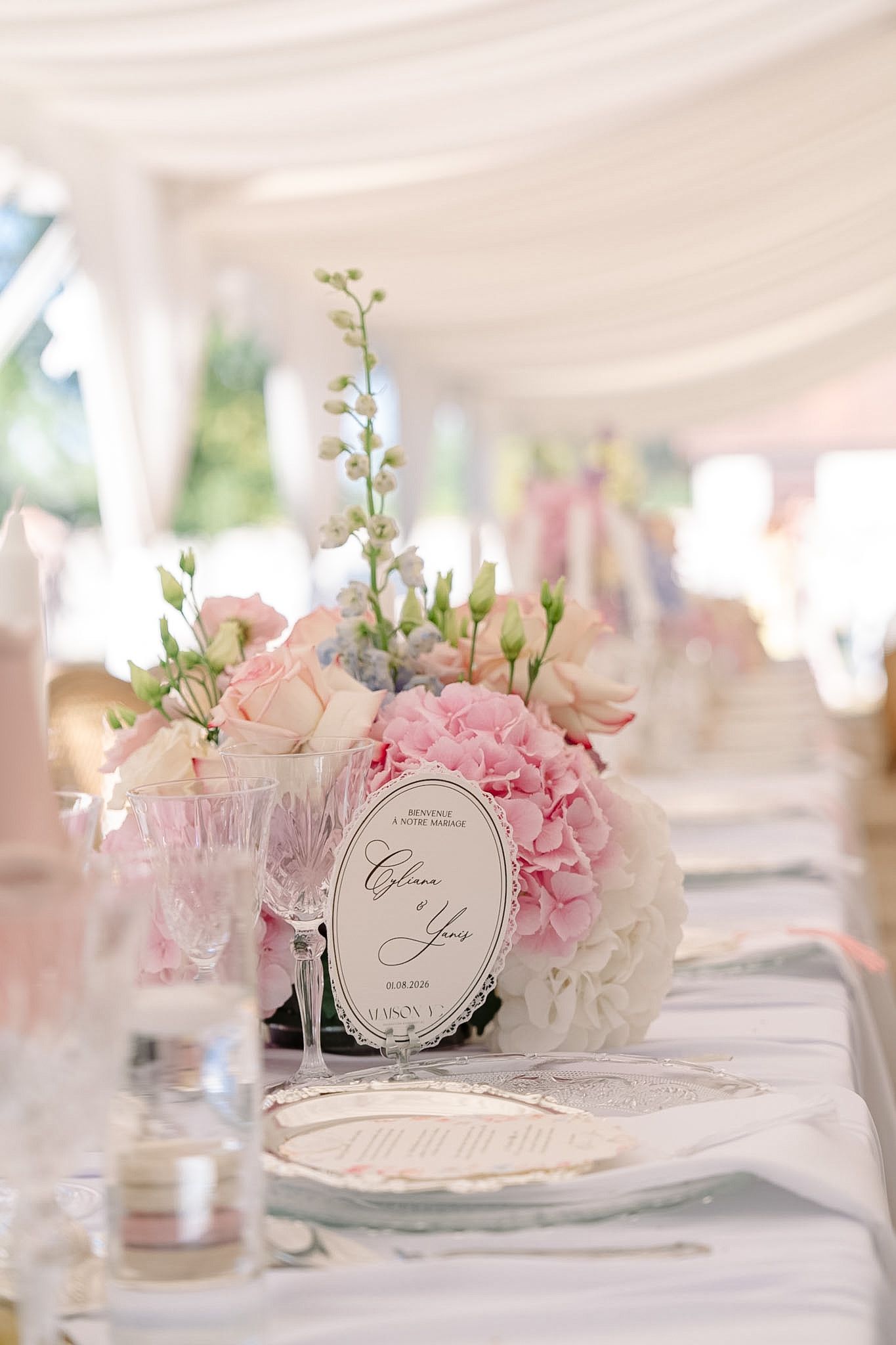 Elegant wedding table with pink hydrangea centerpiece, crystal glasses, and white draping in a romantic reception venue.