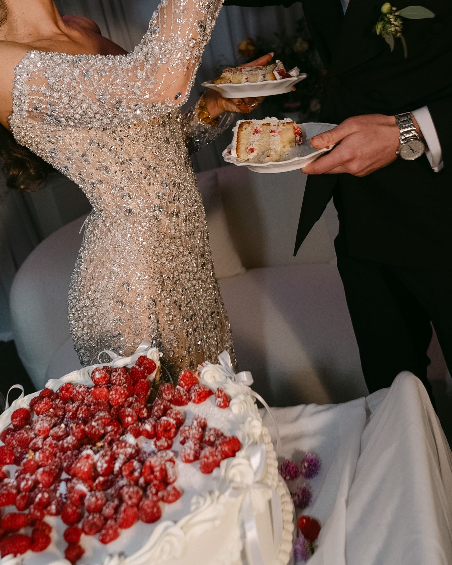 Bride in beaded gown and groom cutting a white wedding cake topped with fresh strawberries at elegant reception.