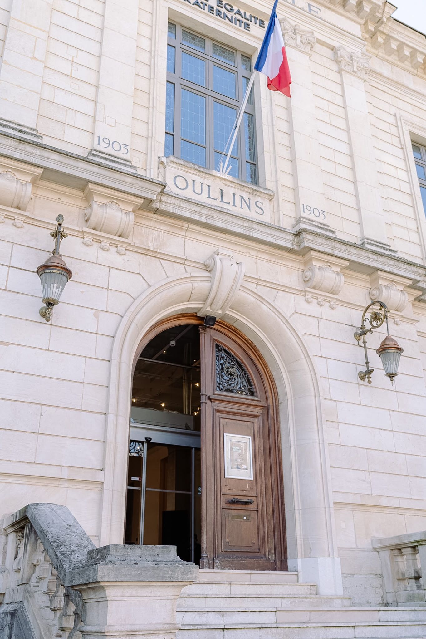 Historic Oullins town hall building facade with French flag and arched wooden entrance door.
