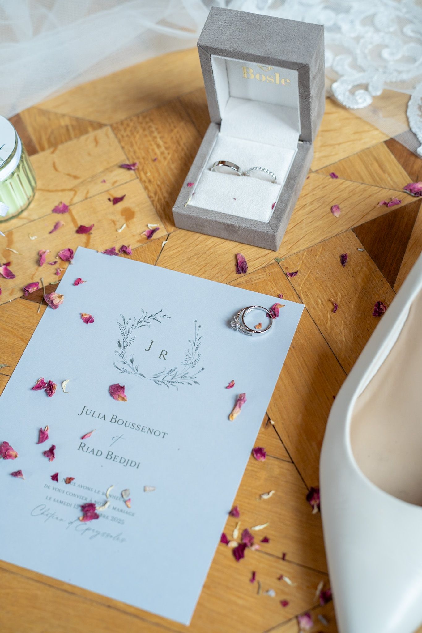 Wedding invitation cards decorated with scattered pink flower petals next to white bridal shoes.