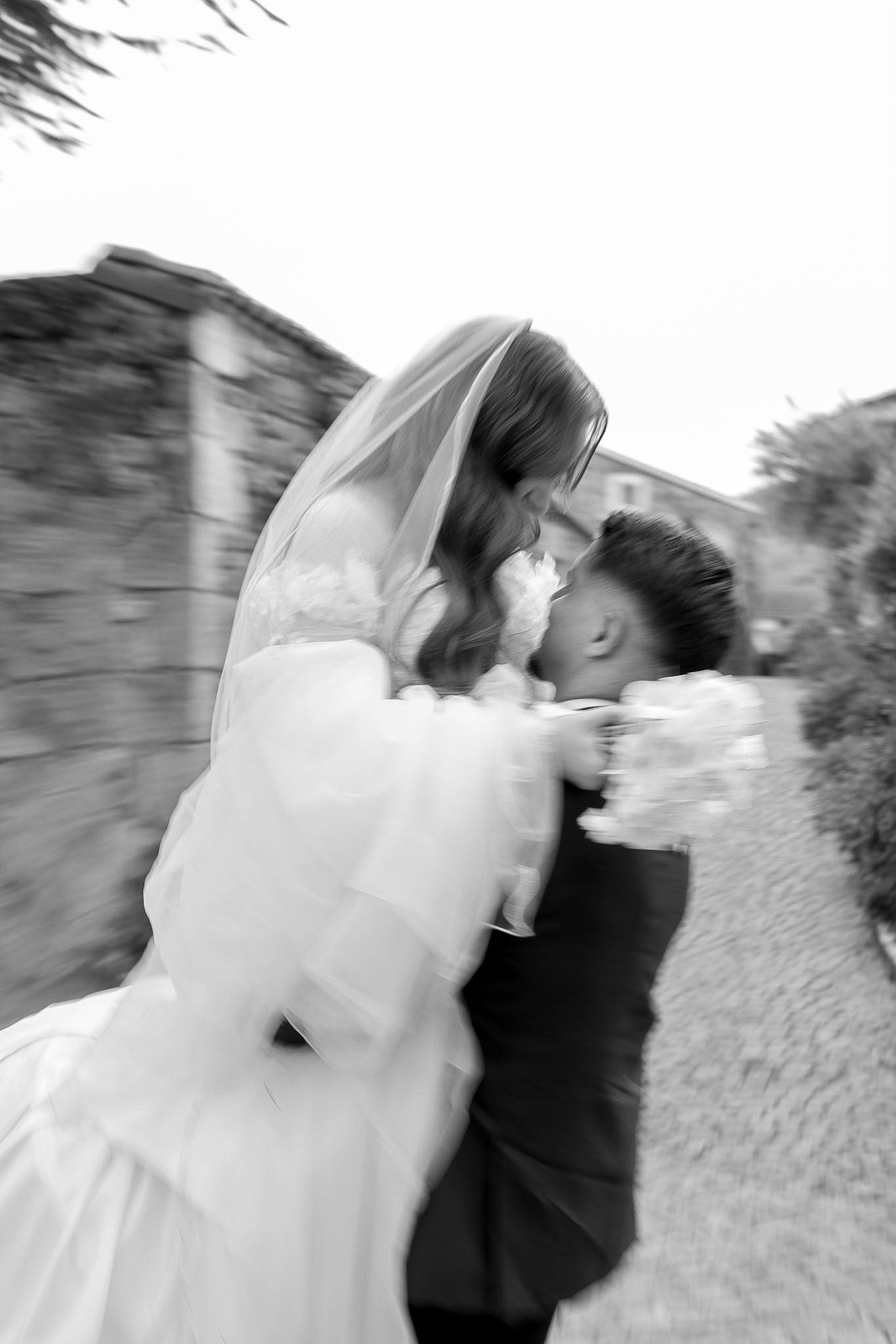 Black and white photo of a bride and groom sharing a romantic kiss, bride holding bouquet, motion blur effect.