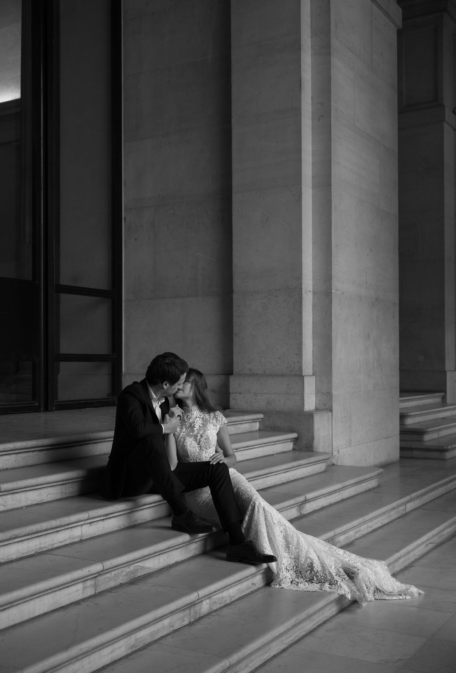 Black and white photo of a couple kissing on grand stone steps with tall columns at their wedding.