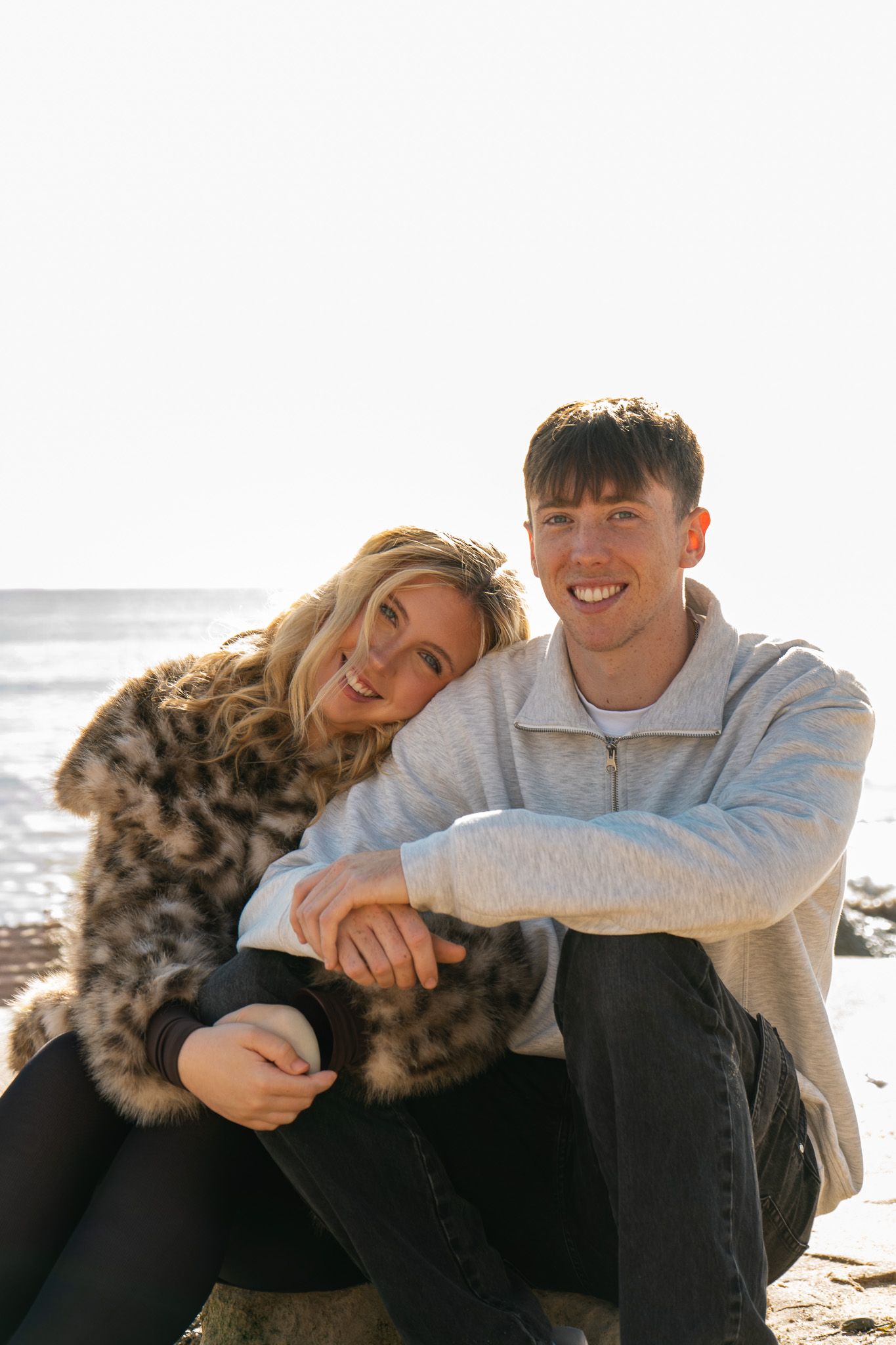 Cam resting her head on Dom's shoulder, both sat on the beach.