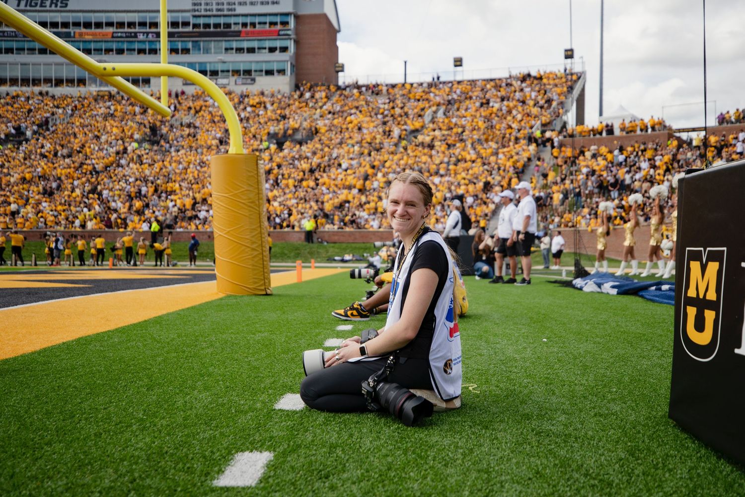 Football field with yellow goal posts and packed stadium stands in bright sunlight.