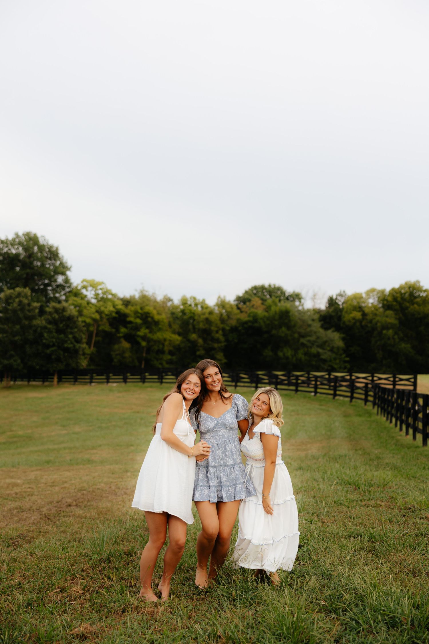 Friends enjoying a moment together in a field with wooden fencing in background.