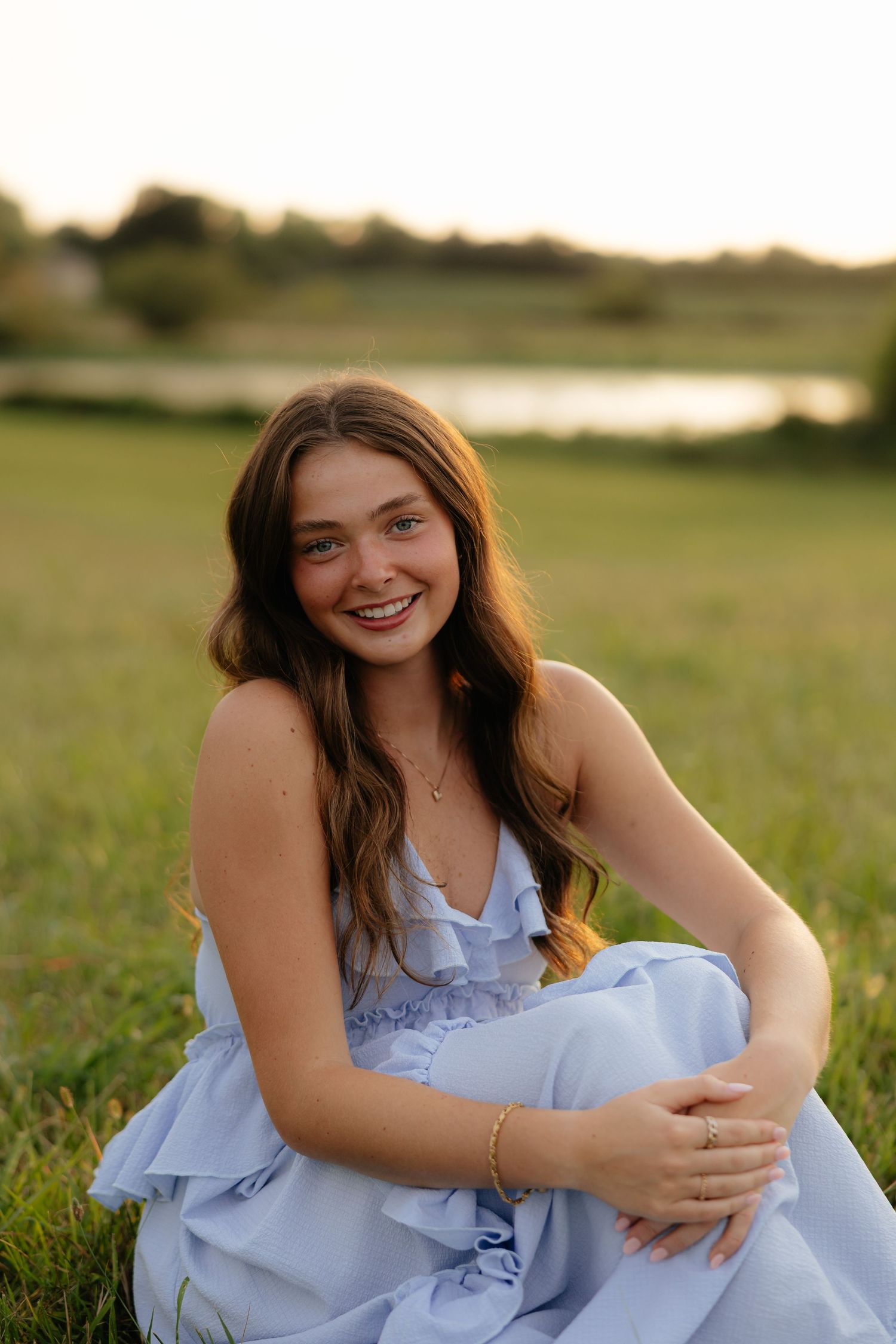 A series of outdoor portraits showing someone in a light blue dress sitting in a grassy field at sunset.