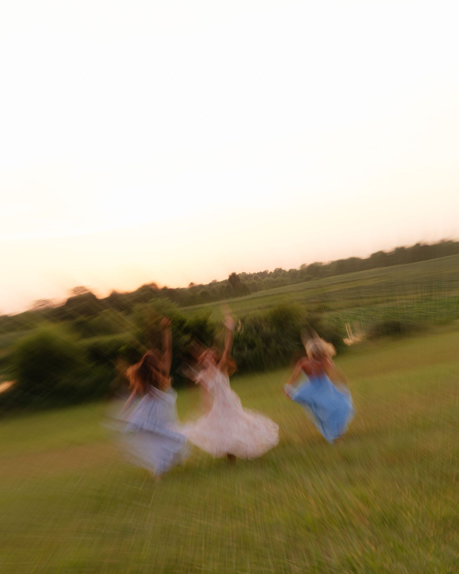 Motion-blurred figures roll down a grassy hill at sunset creating an artistic effect.