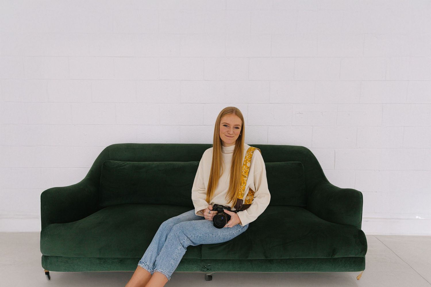 Person in cream sweater poses on dark green vintage couch during photo session.