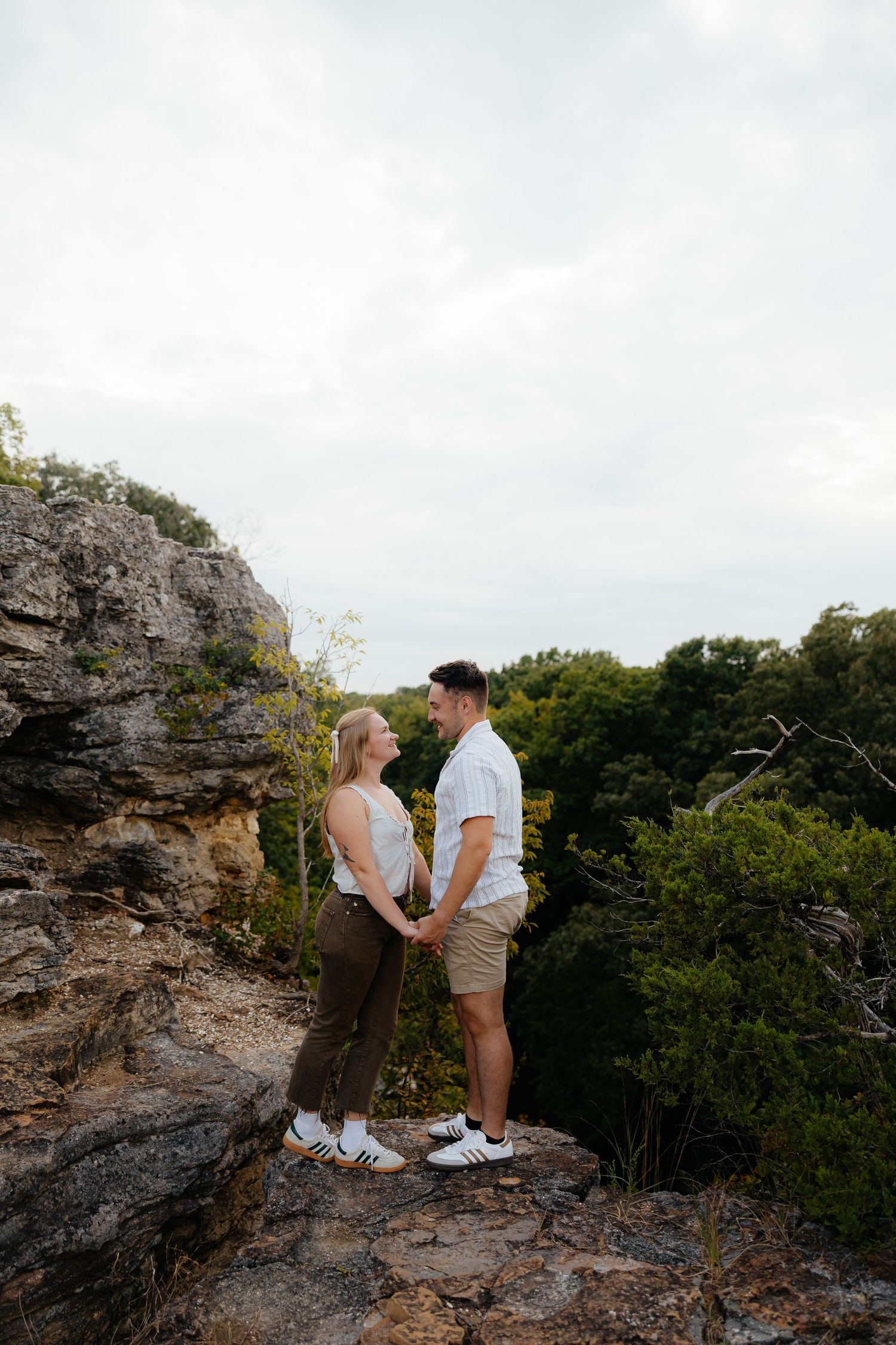 Couple shares tender moment on rocky cliff overlook surrounded by lush vegetation.