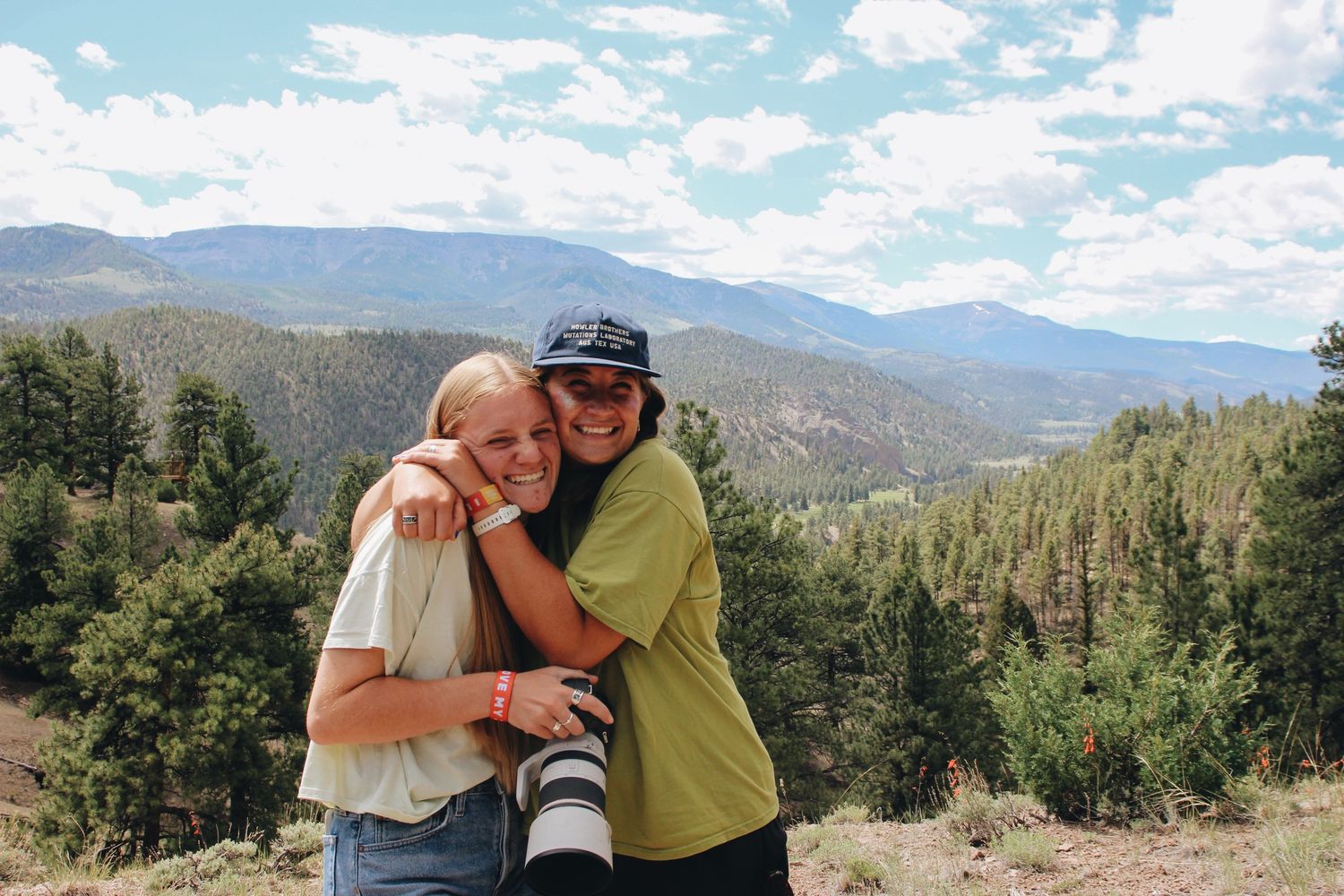 Couple embraces while hiking in scenic mountain landscape with dramatic clouds and evergreen trees.