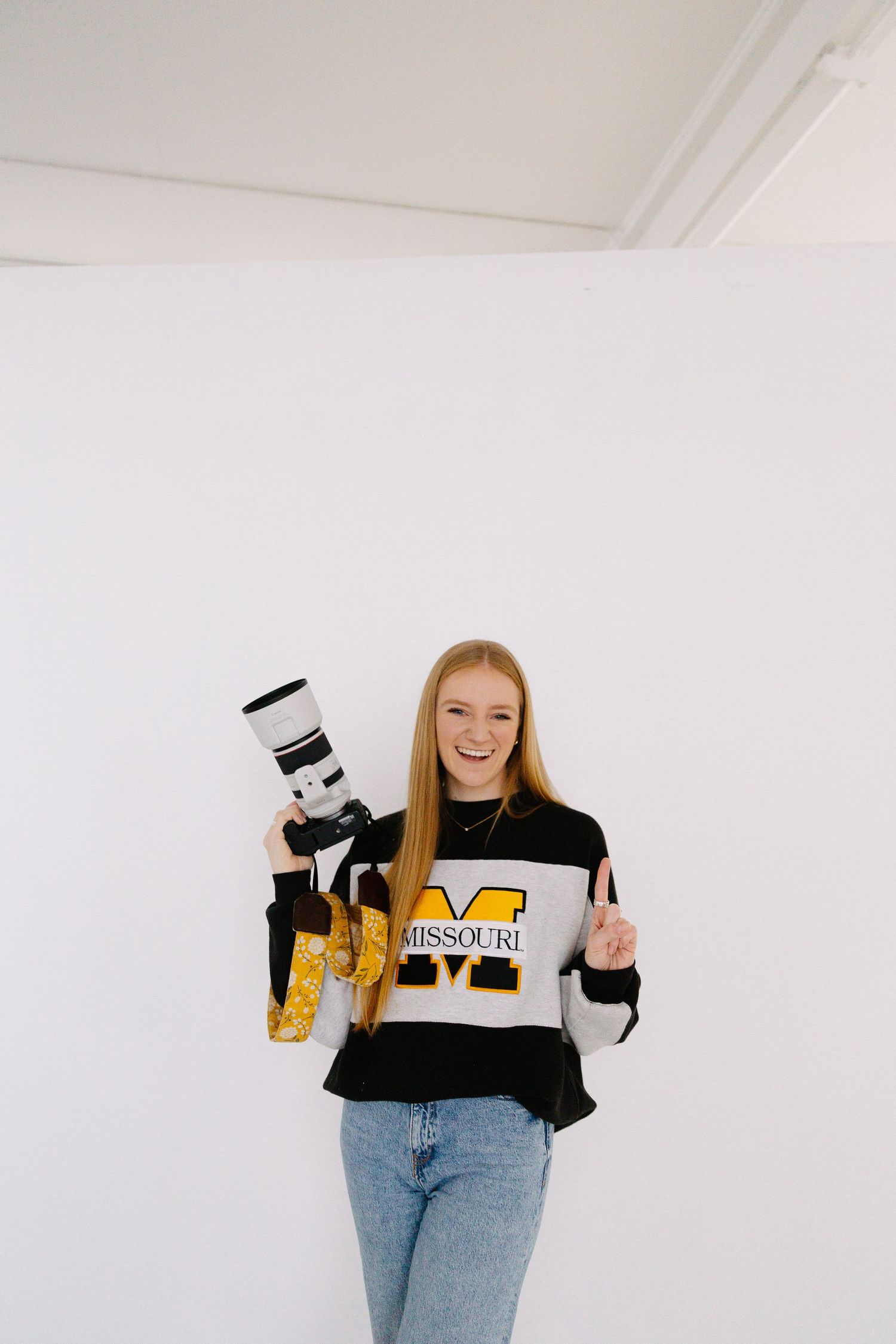 Person in Missouri sweatshirt and jeans poses with props against white wall.