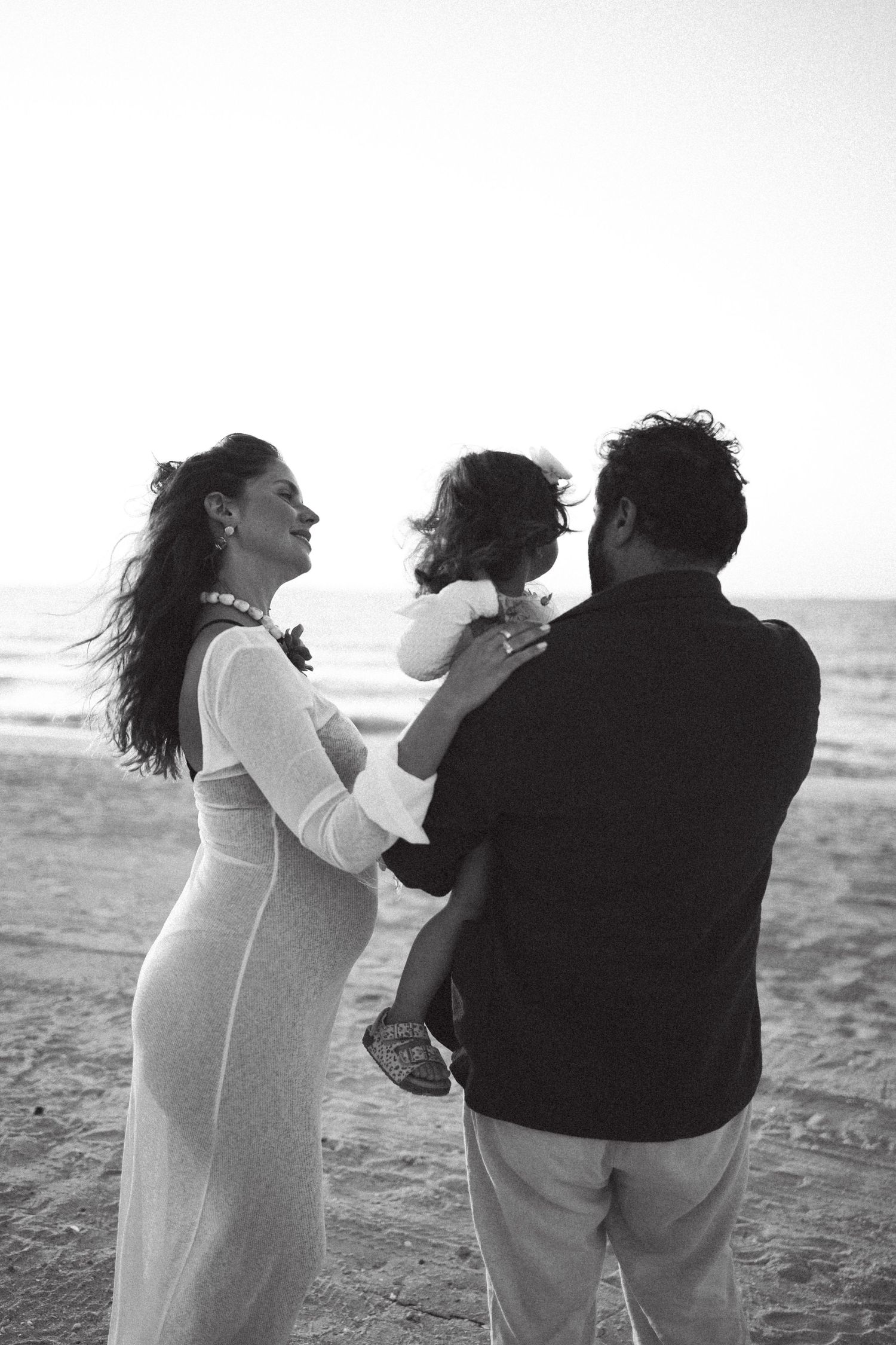 Family shares tender moment together on beach at sunset during maternity session.
