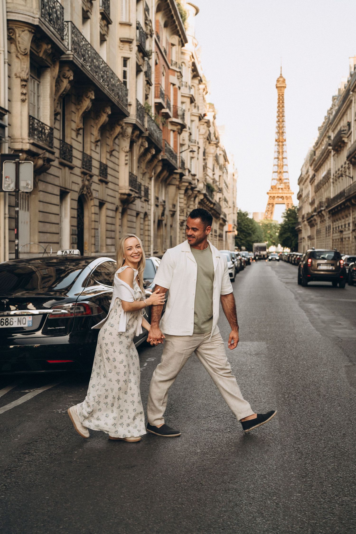 Couple walking hand-in-hand on a Parisian street with the Eiffel Tower glowing in the background at sunset.