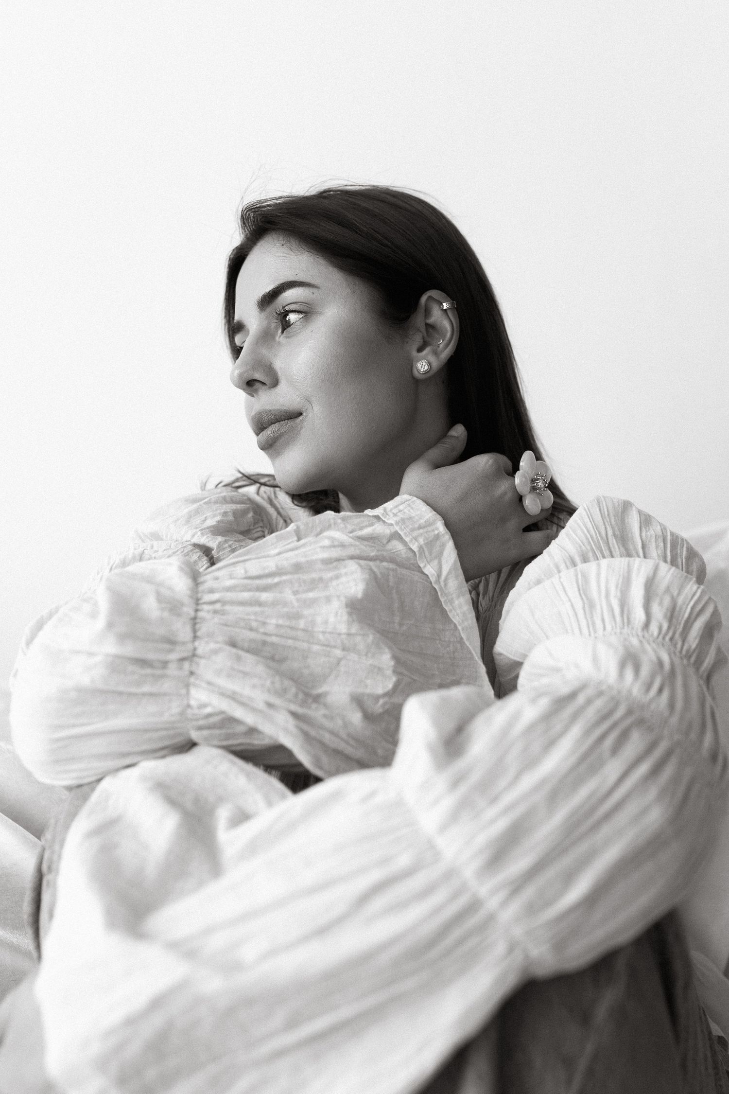 Black and white portrait of a young woman with dark hair, wearing a white linen dress, sitting and gazing thoughtfully.
