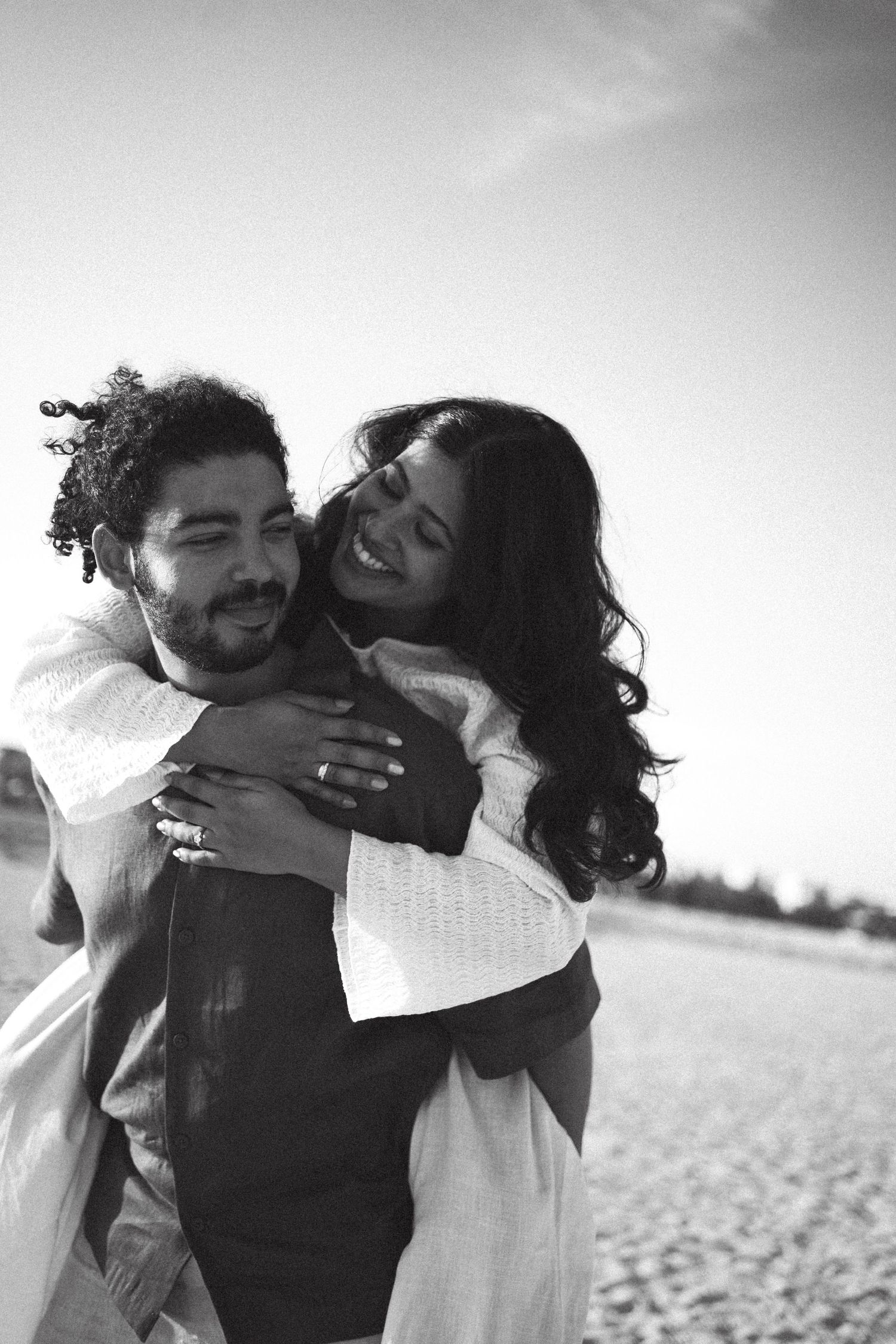 A couple laughing and embracing on a beach in black and white photography.