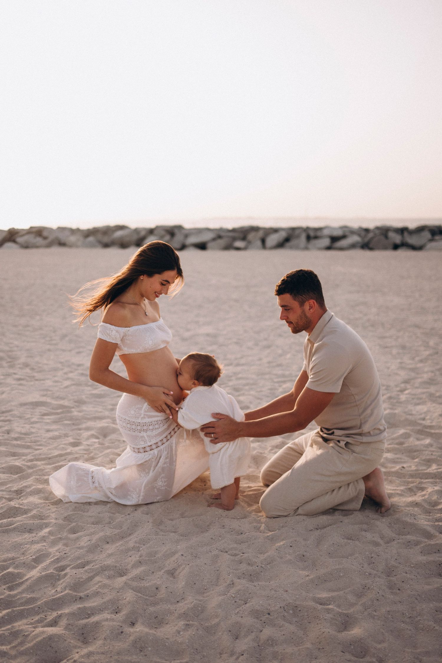 Family sharing tender moment together on sandy beach at sunset in white outfits.