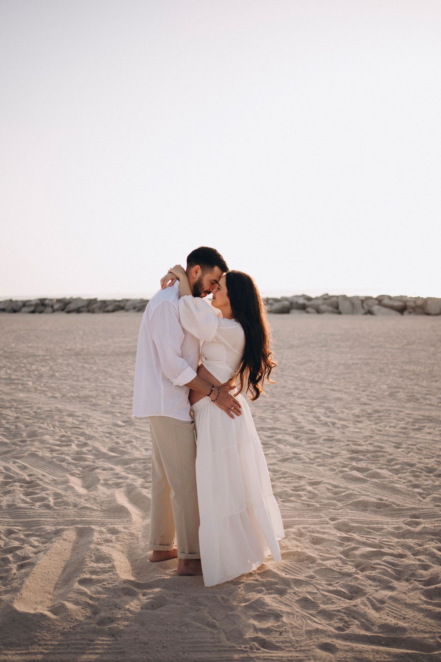 Romantic couple in white clothing share intimate moment on desert sand dunes.