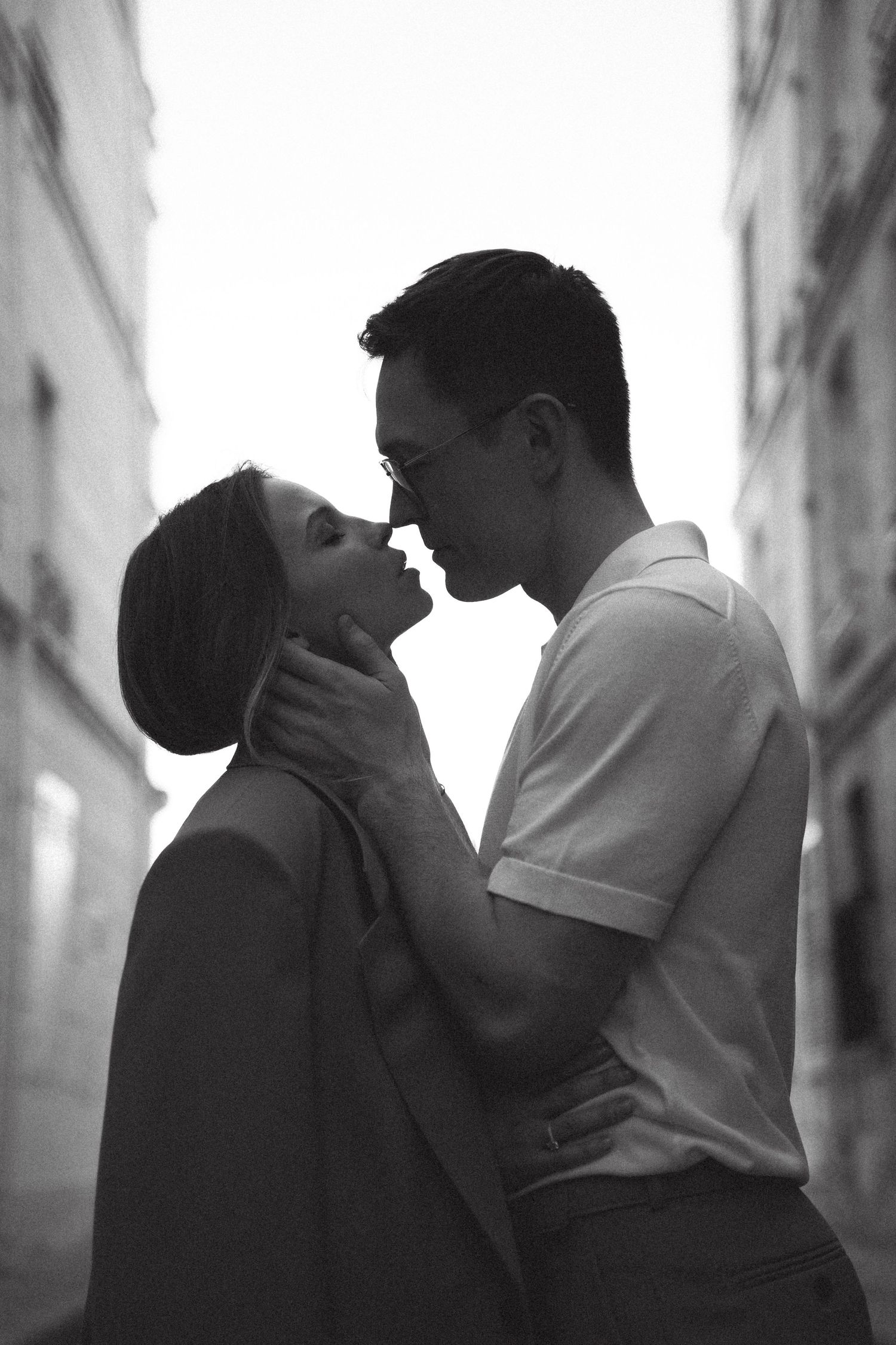 Black and white photo of a romantic couple almost kissing on a European city street, the man tenderly holding the womans face.