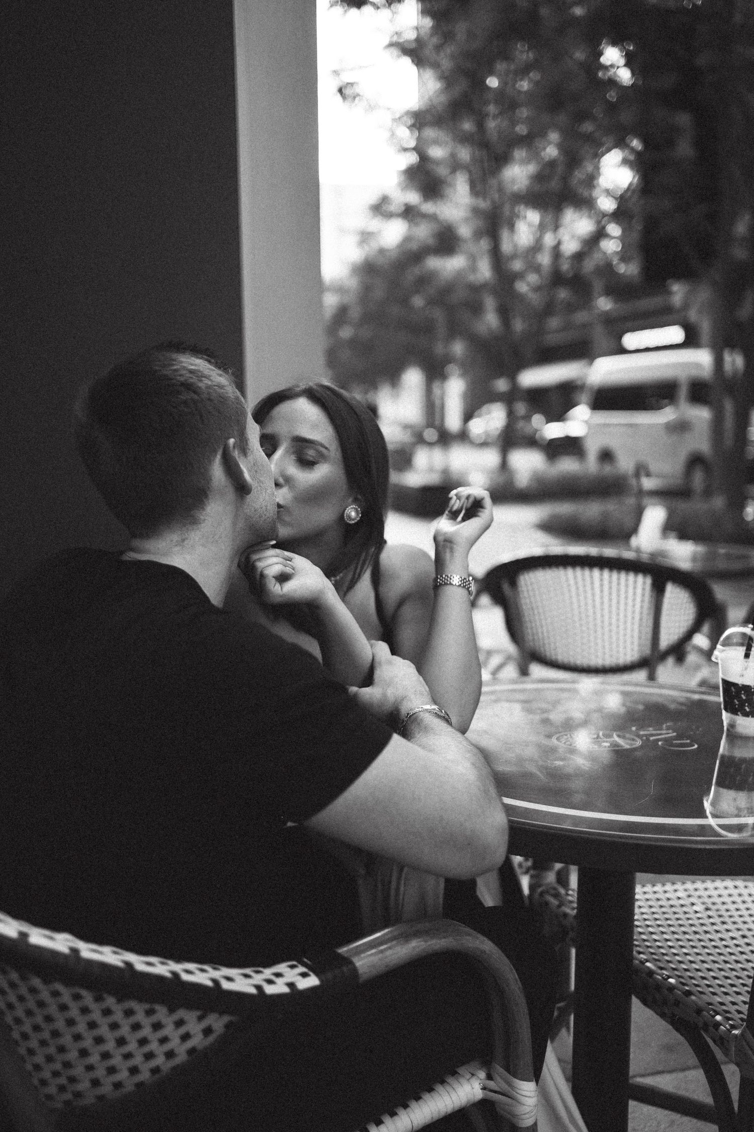 An intimate black and white photo of a couple sharing a moment at an outdoor cafe.