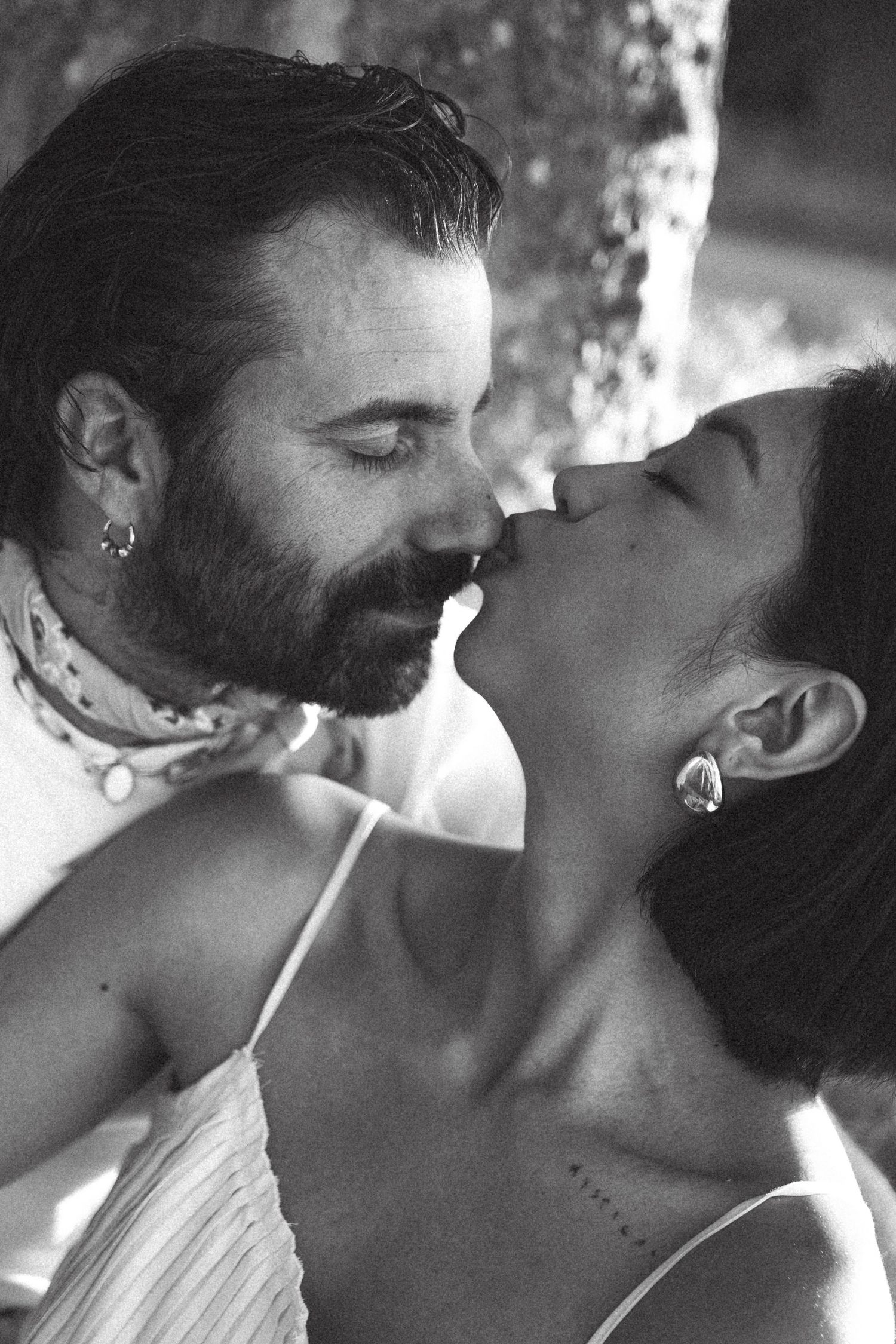 Black and white photo of a bearded man and woman sharing a romantic kiss outdoors.