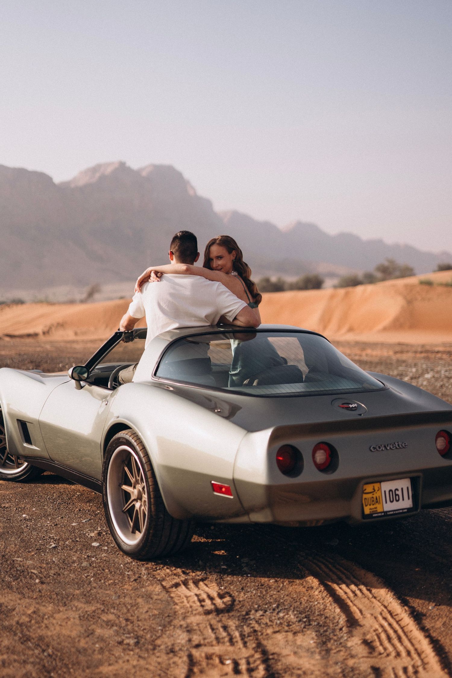 Classic Corvette parked in desert landscape with mountains in background during sunset.