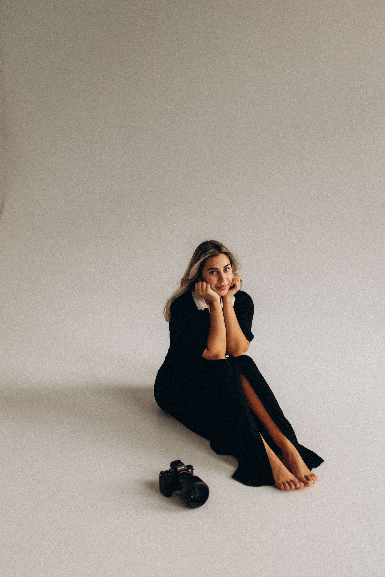 Artistic portrait in minimalist setting with camera on floor and model in flowing black dress.