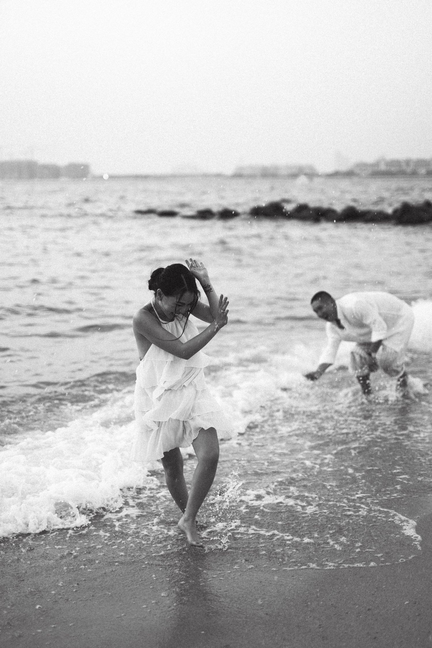 Playful couple splashing in ocean waves wearing white clothing.