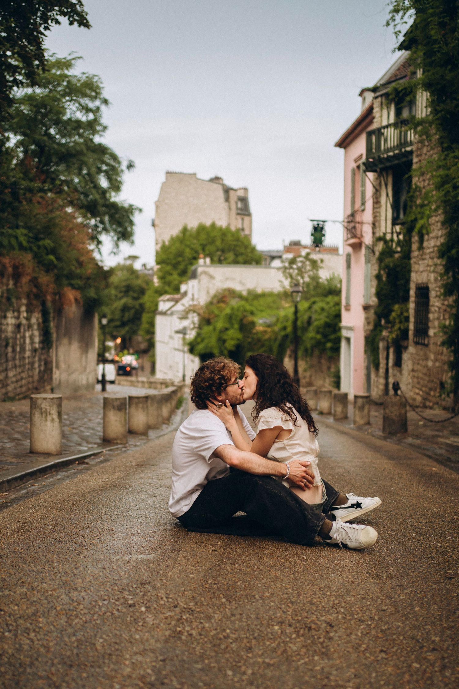 Romantic couple kissing while sitting on a cobblestone street in Montmartre, Paris, surrounded by charming buildings.