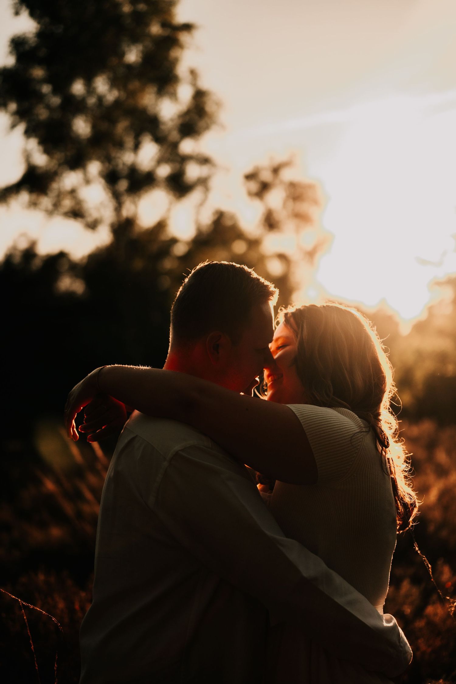 A silhouette of a couple embracing at sunset with golden light creating a warm backlit glow through trees.