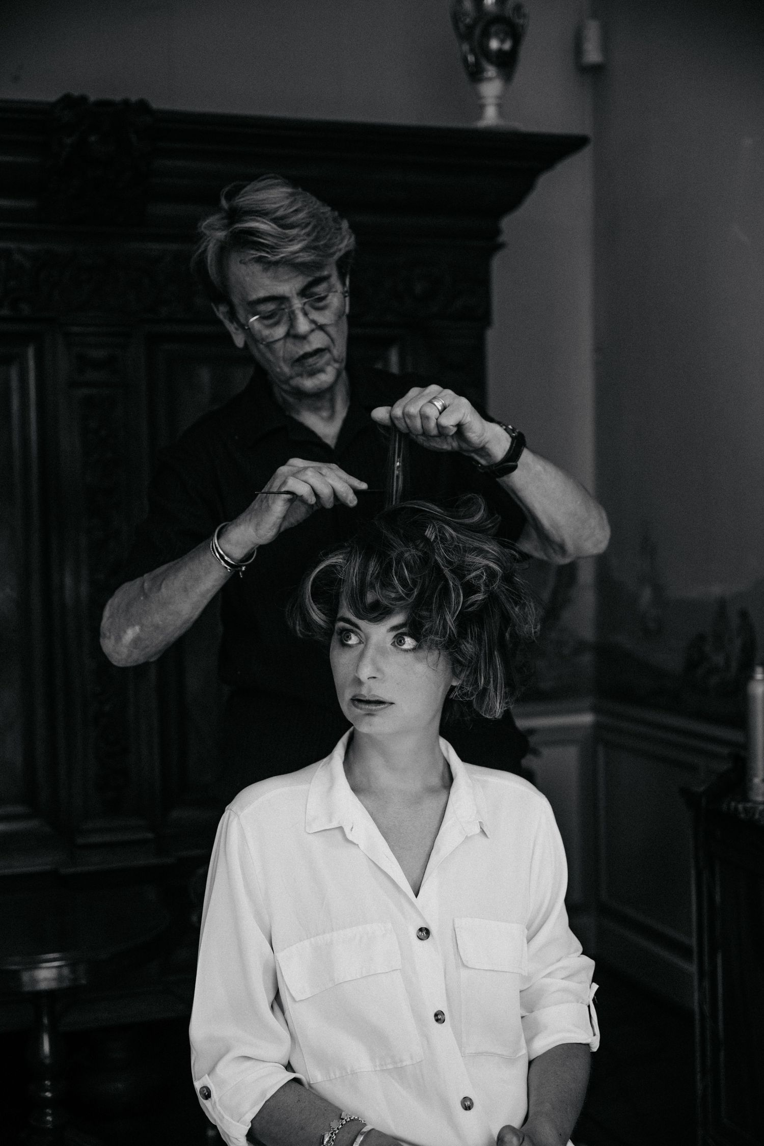 A black and white photograph of a hairstylist working on styling a client's hair in a vintage setting.