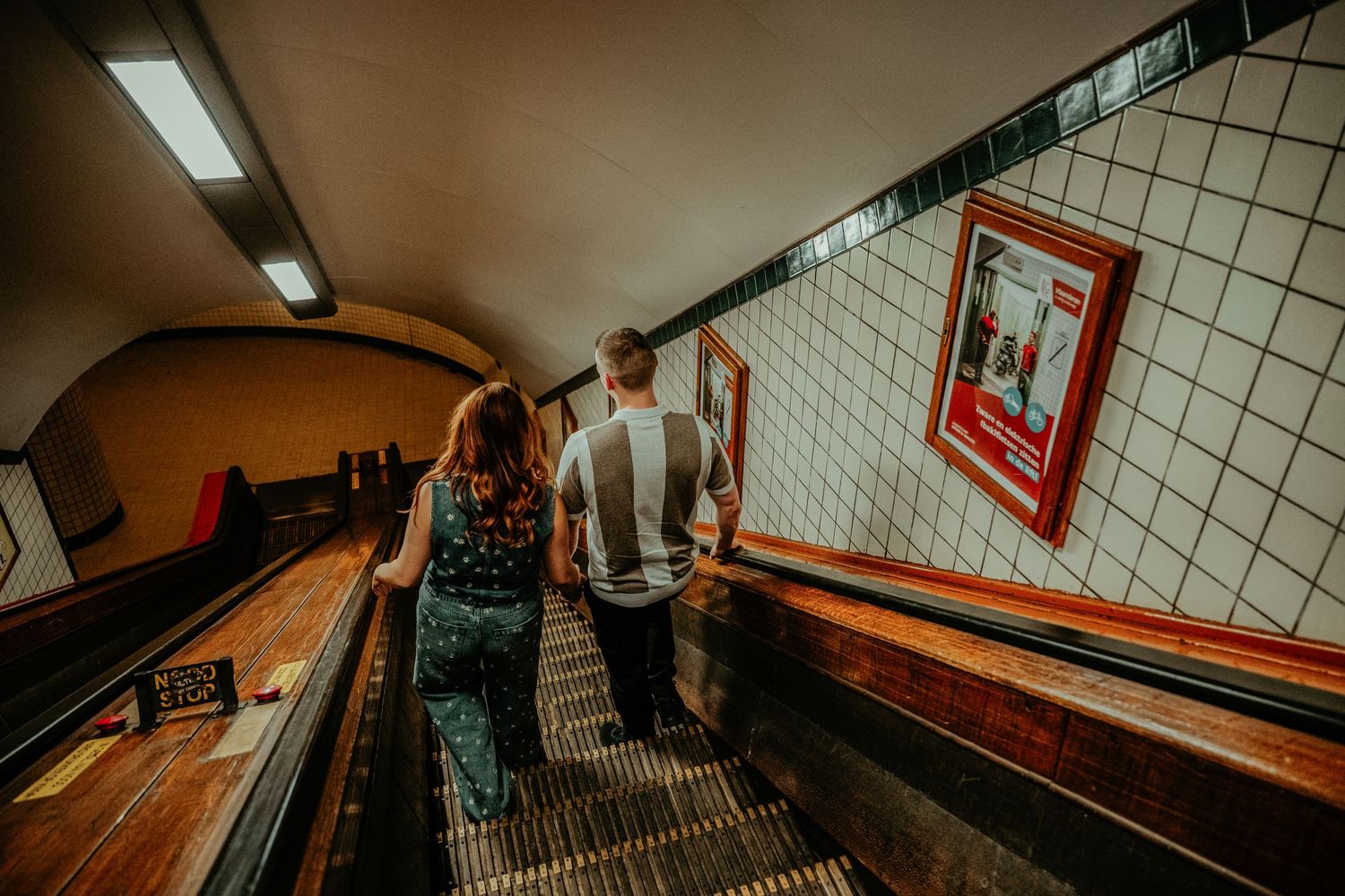 A dark tiled subway tunnel hallway with fluorescent lights and white walls stretches into the distance.