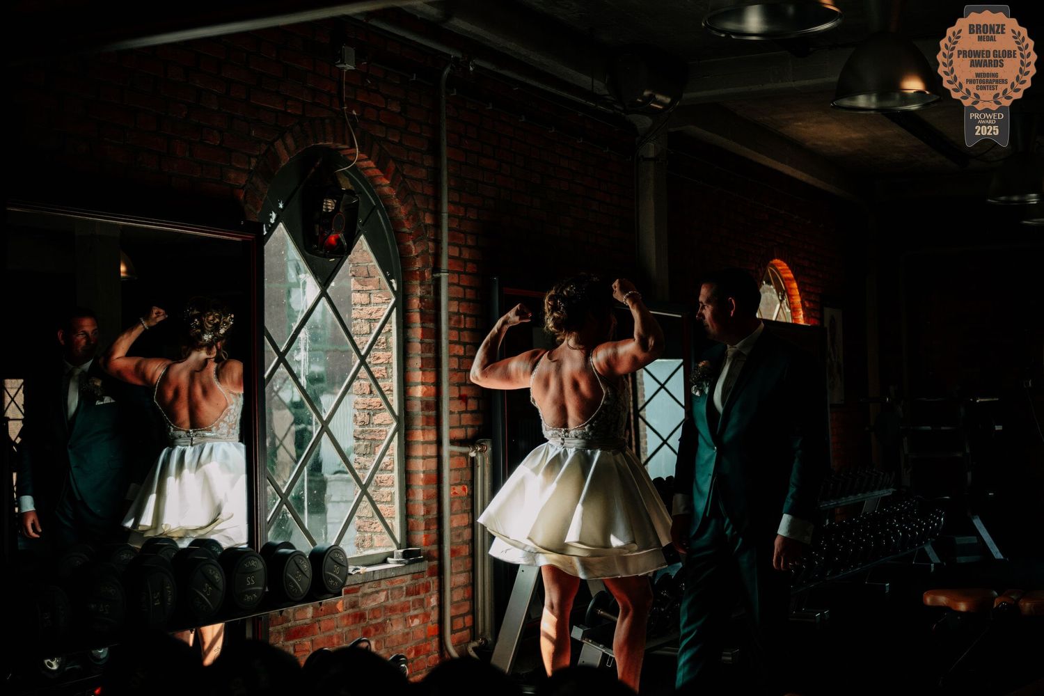 Wedding guests dance and celebrate together in a dimly lit reception venue with diamond-paned windows.