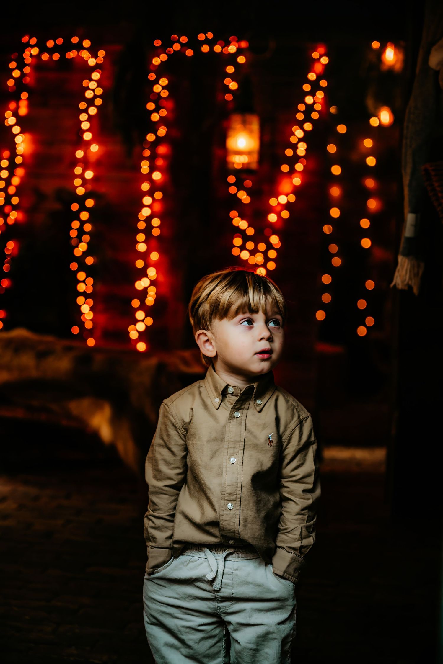A child in a beige button-down shirt sits against a dark background with glowing orange holiday lights.