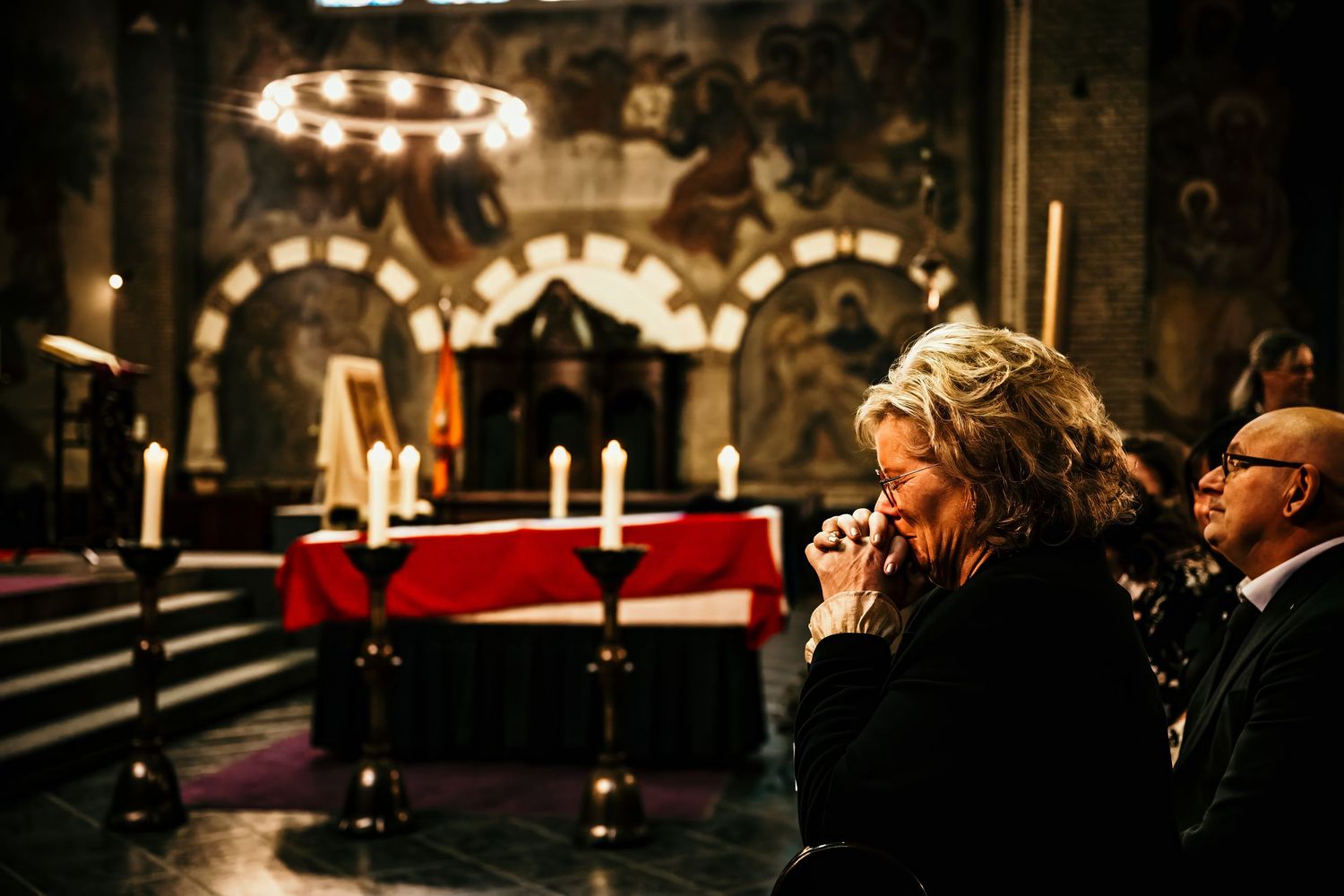A dimly lit cathedral interior with ornate architecture and glowing chandeliers creates a dramatic atmosphere.